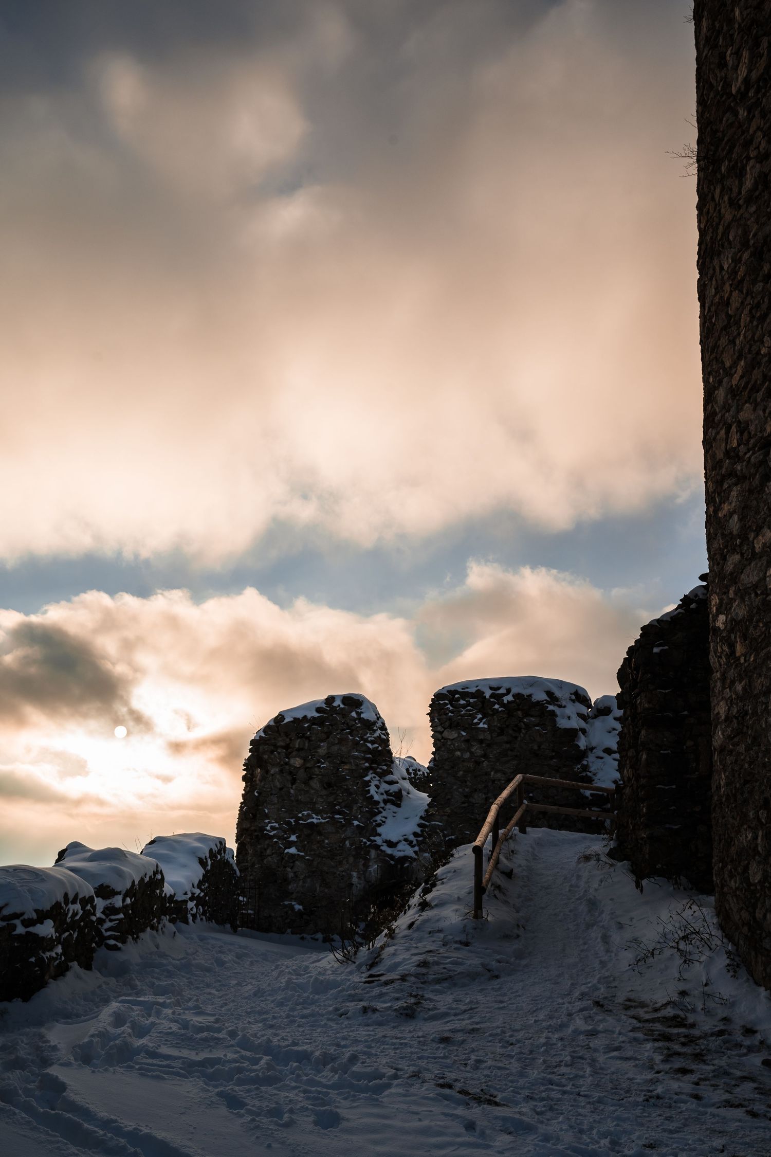 Snow-covered castle walls silhouetted against a dramatic sunset sky.