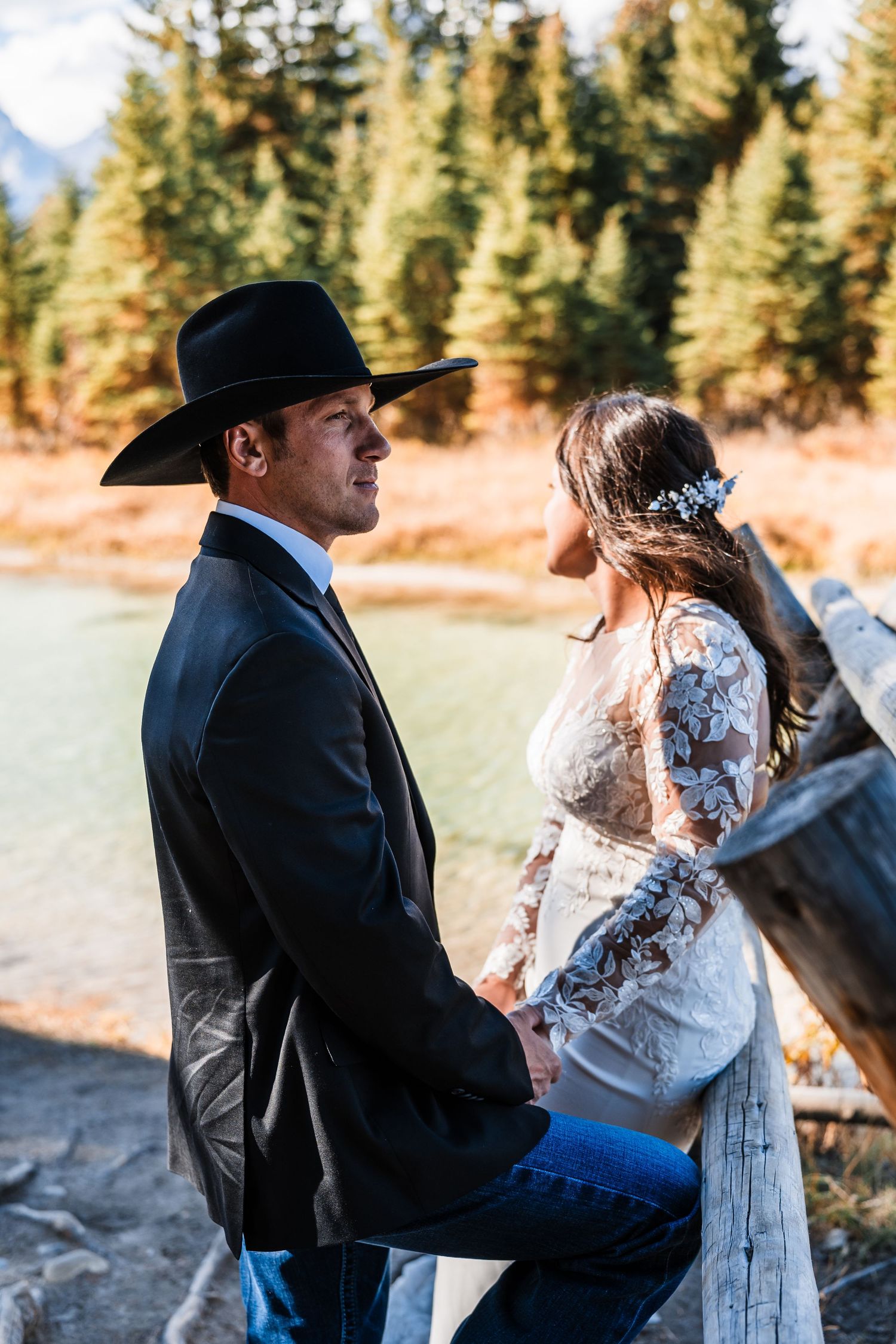 A couple in western attire shares tender moments during an outdoor photo session in a forest setting.