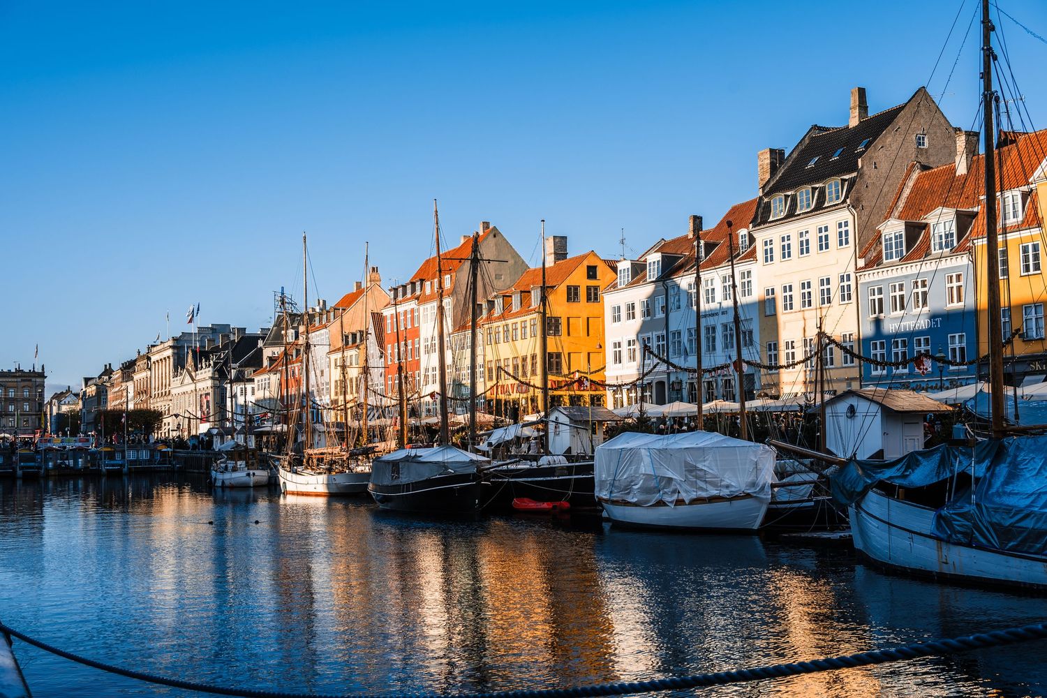 Scenic panoramic view of colorful historic buildings along Nyhavn canal in Copenhagen at sunset with boats and reflections.