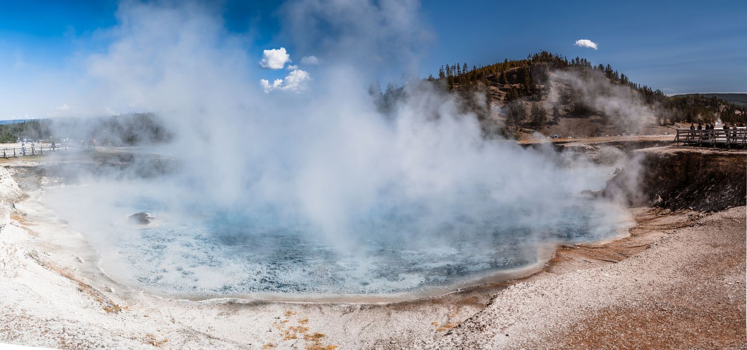 Steaming geothermal pool at Yellowstone National Park with bright blue water and mineral deposits.