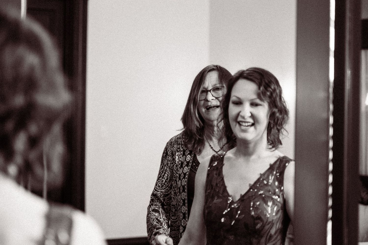 Black and white photo of bride smiling with mother helping her get ready before wedding ceremony.