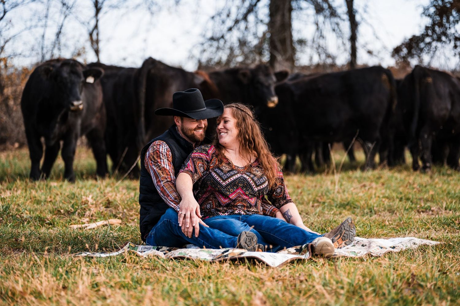 A couple lounges together on a grassy field during a romantic outdoor photoshoot session.