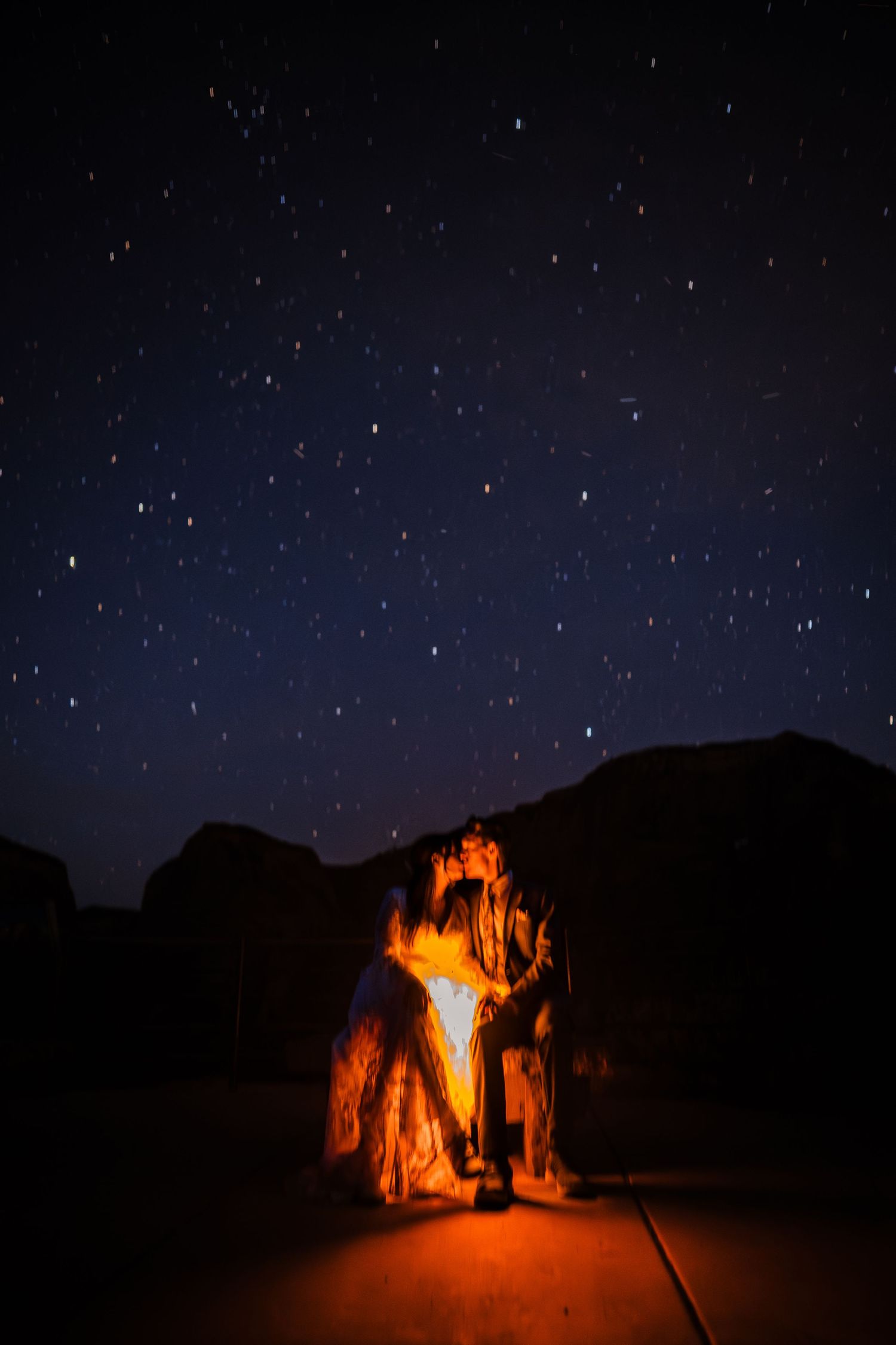 Couple silhouetted under glowing rock arch beneath stunning starry night sky landscape.
