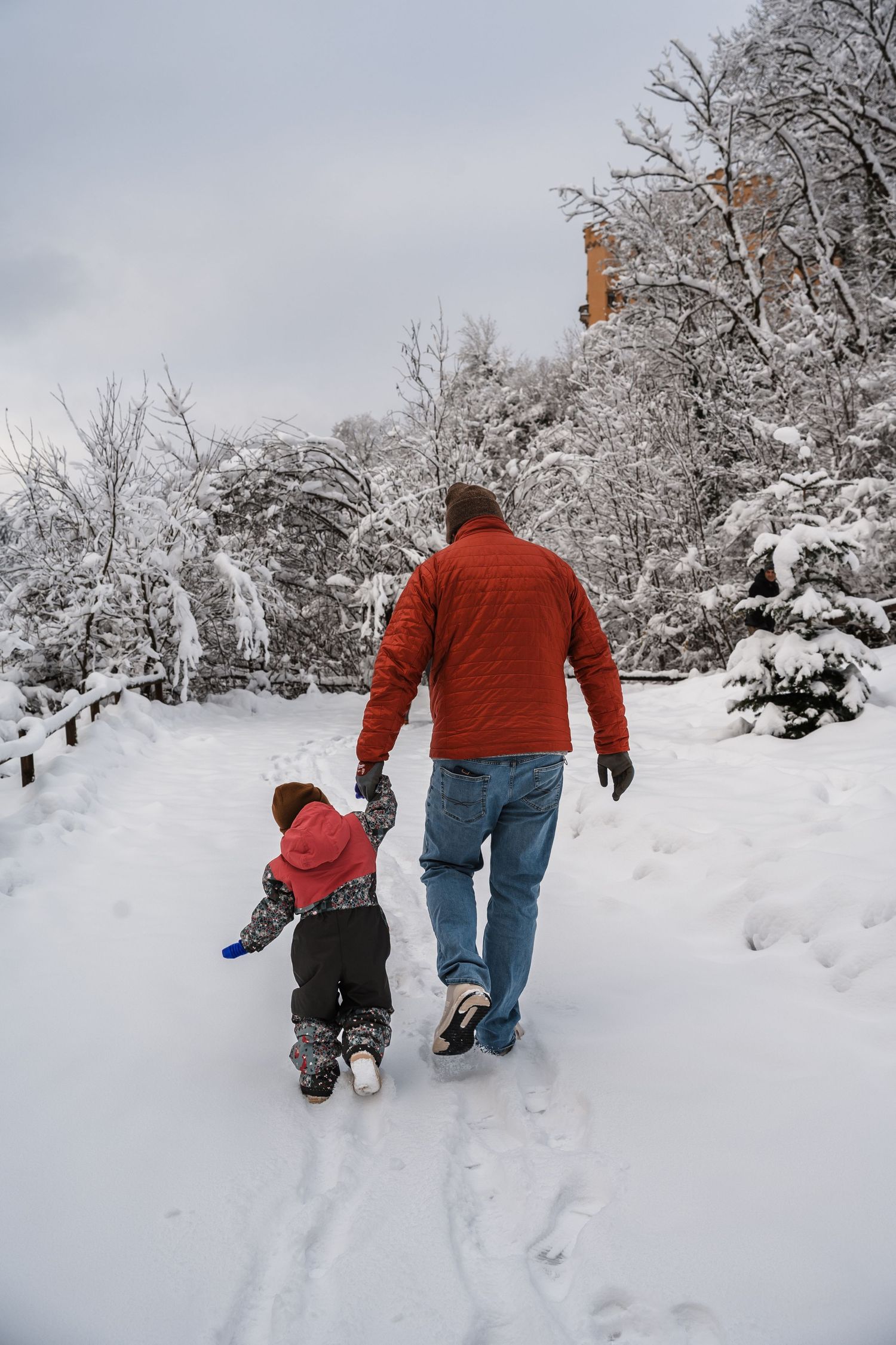 Two people walk together through a snowy winter landscape with snow-covered trees lining their path.