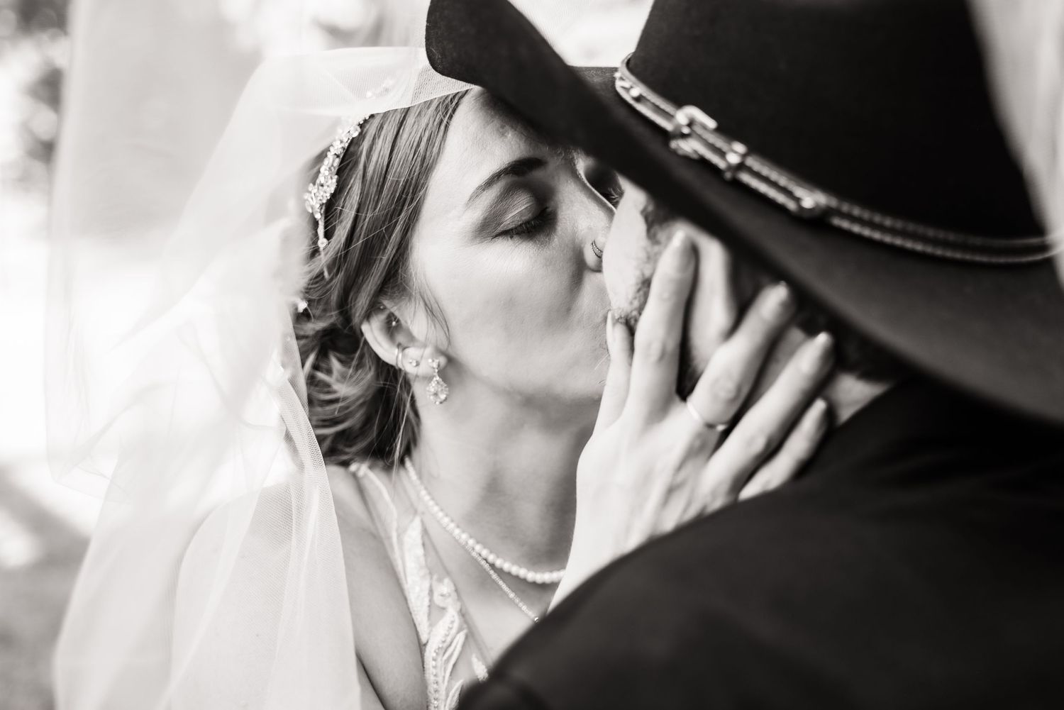 A romantic black and white portrait of a couple sharing an intimate kiss under wide brim hat.