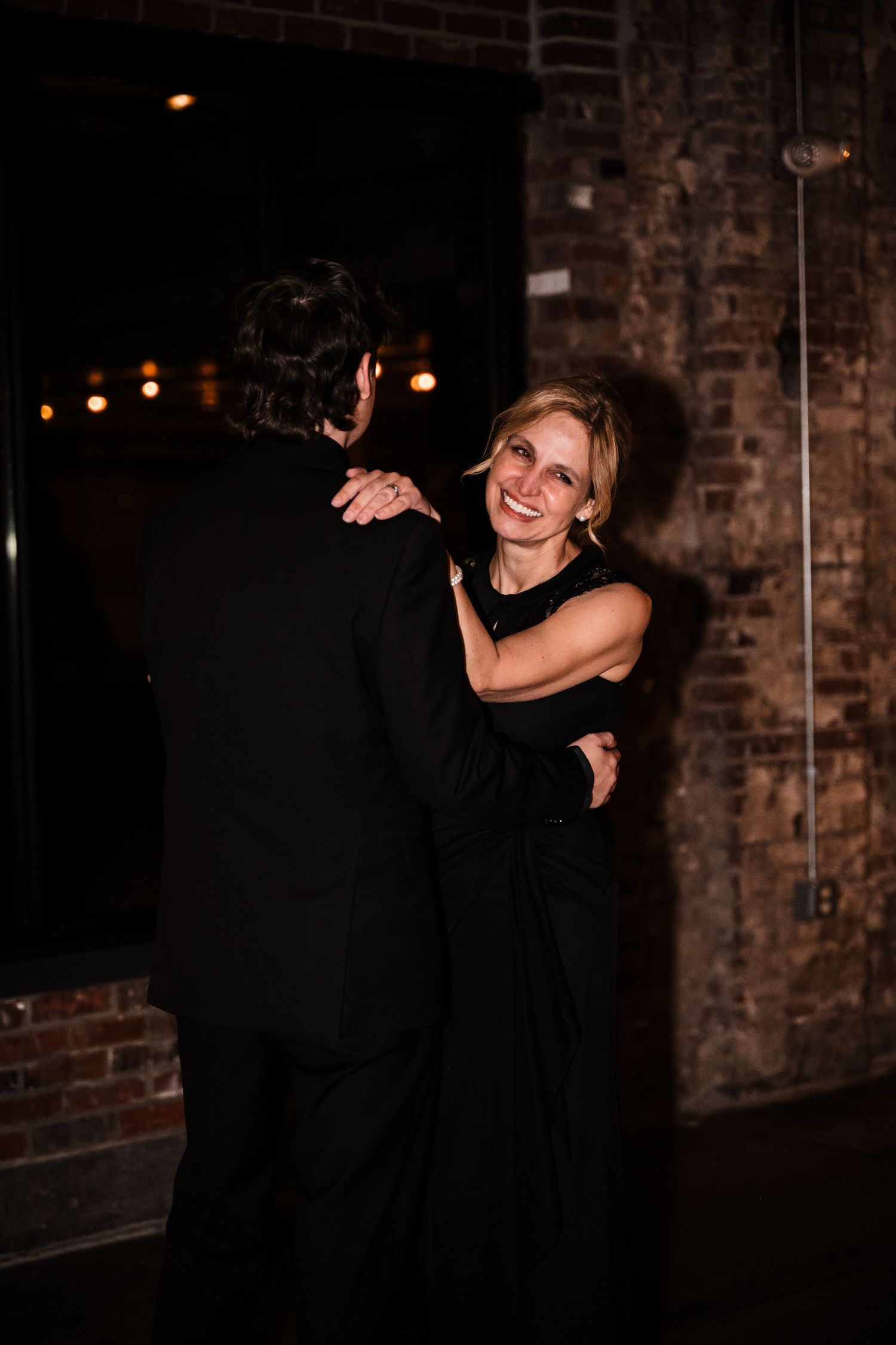 Couple dancing romantically in a dimly lit venue with exposed brick walls and warm lighting.