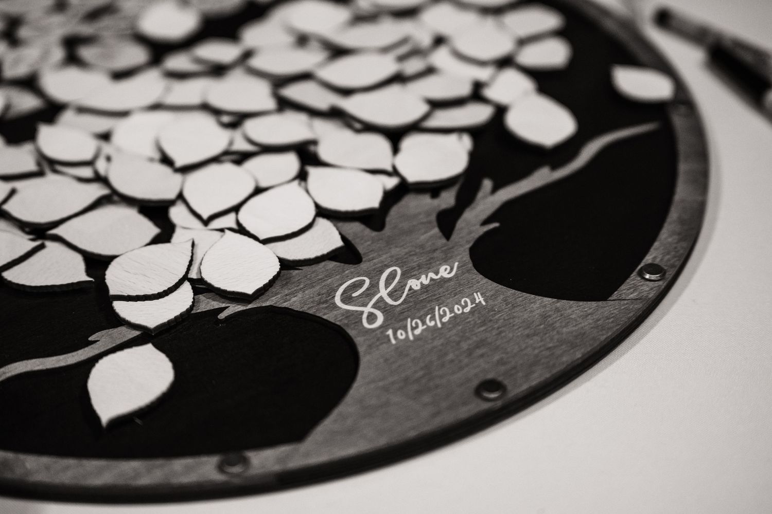 Close-up detail shot of a custom wedding guestbook with laser-cut tree design in black and white.