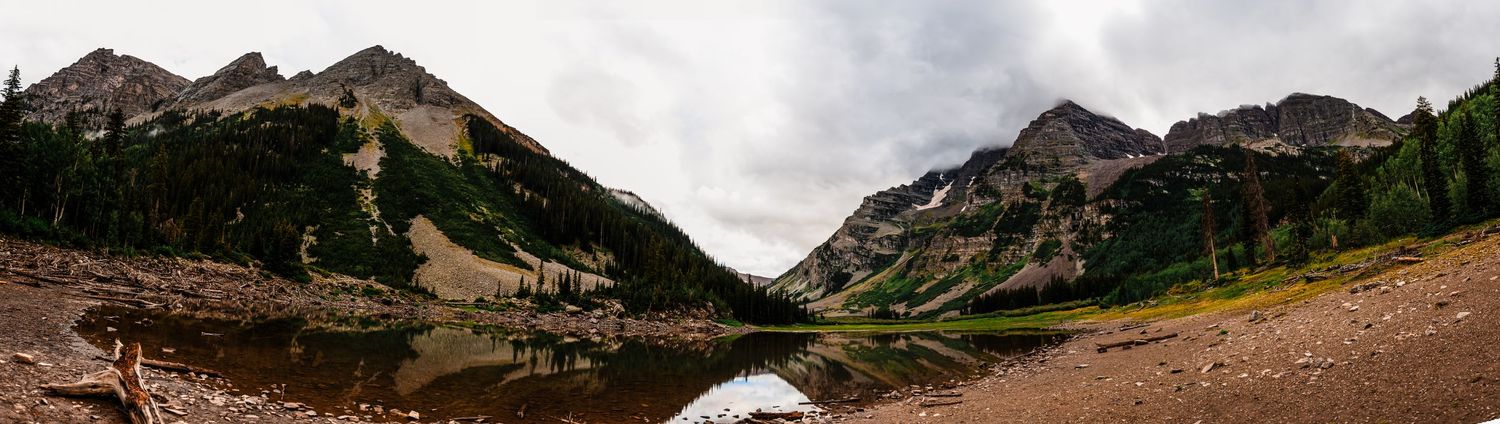 Panoramic view of a mountain lake surrounded by steep peaks and alpine meadows.