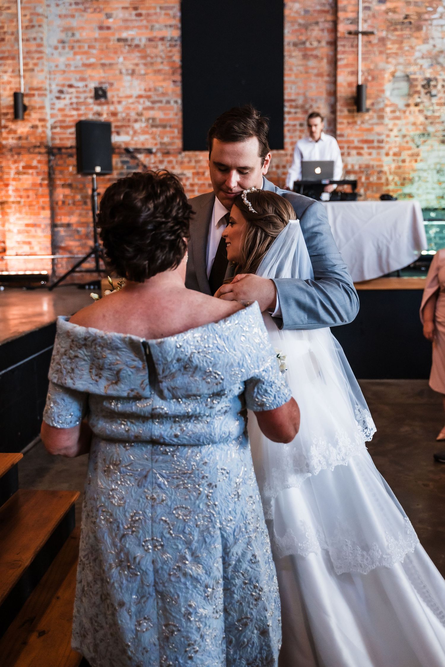 Intimate dance moment at a rustic brick wedding venue with guests and DJ in background.