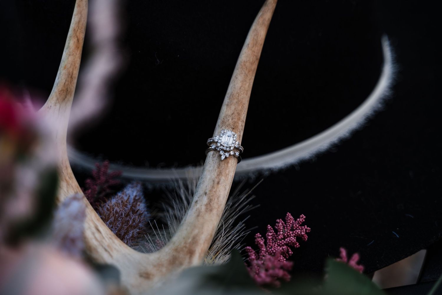 Diamond ring detail shot with delicate pink floral elements against black background.