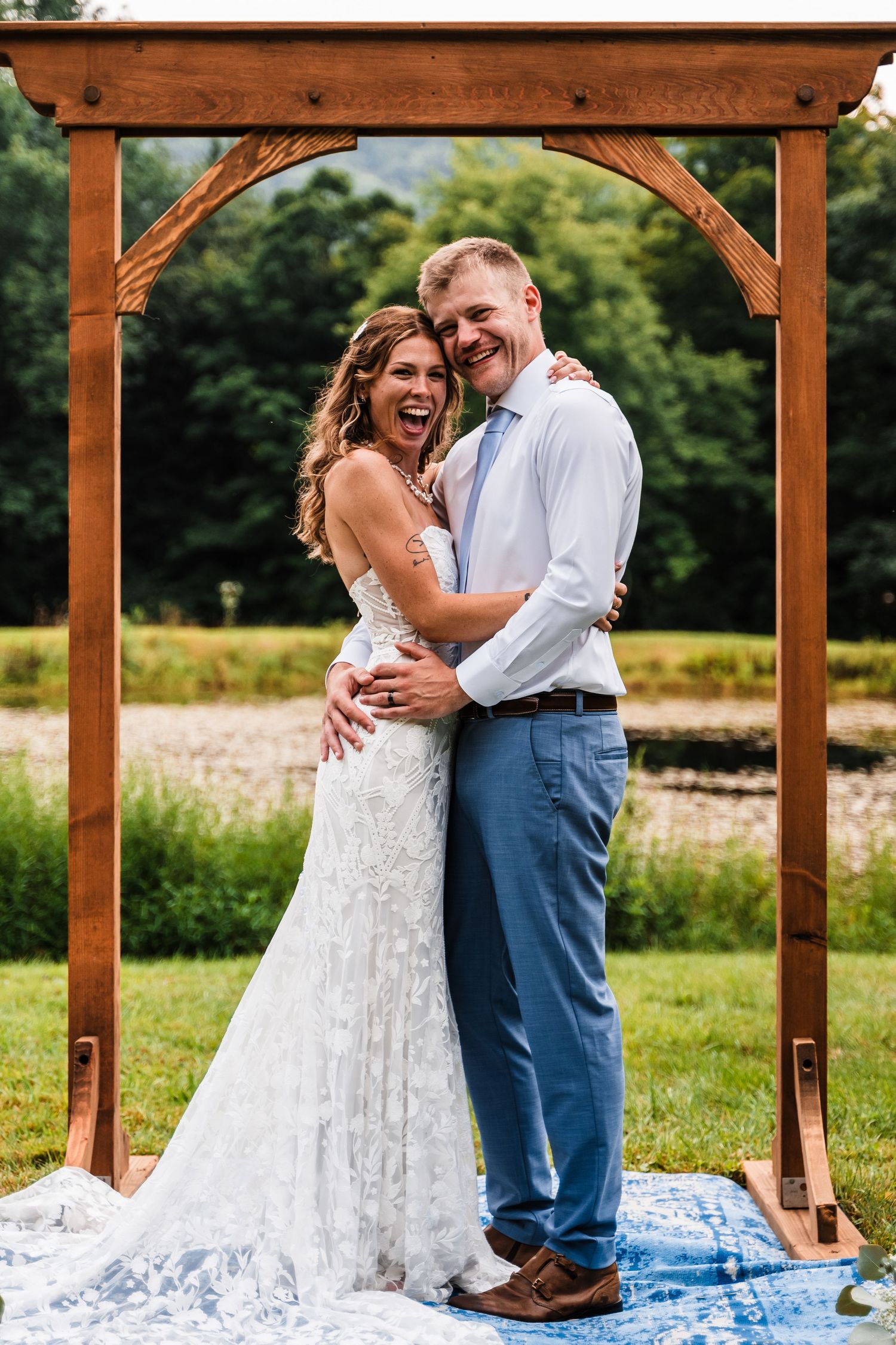 A candid laughing moment captured under a rustic wooden wedding arch during the ceremony.