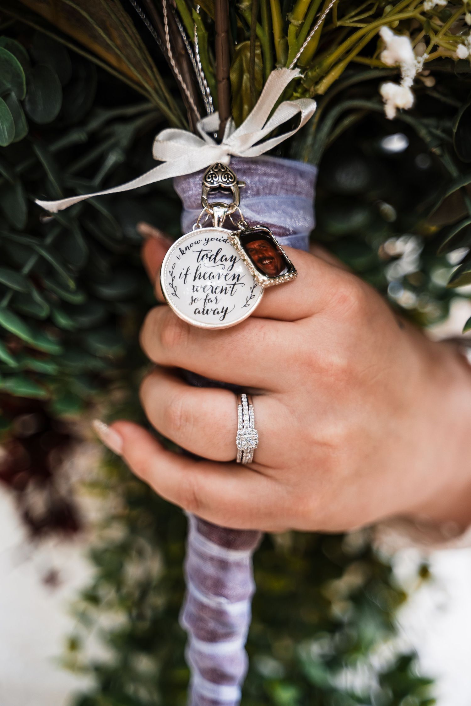 A close-up of a wedding bouquet handle with a decorative charm and engagement ring.