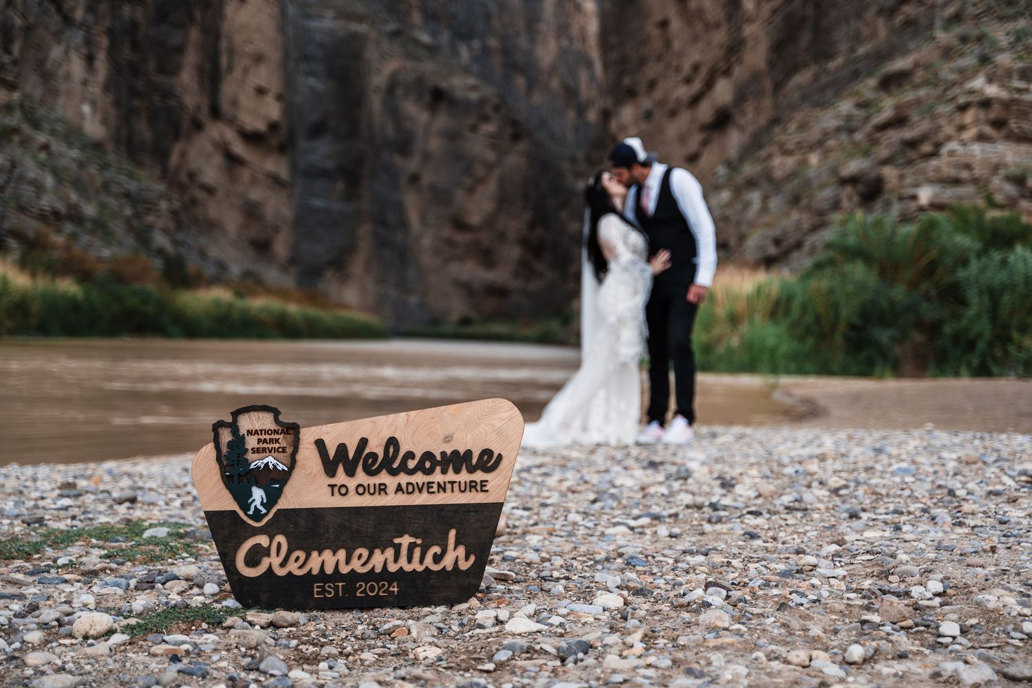 A welcome sign for Clementich sits in foreground with a couple in wedding attire by canyon walls.