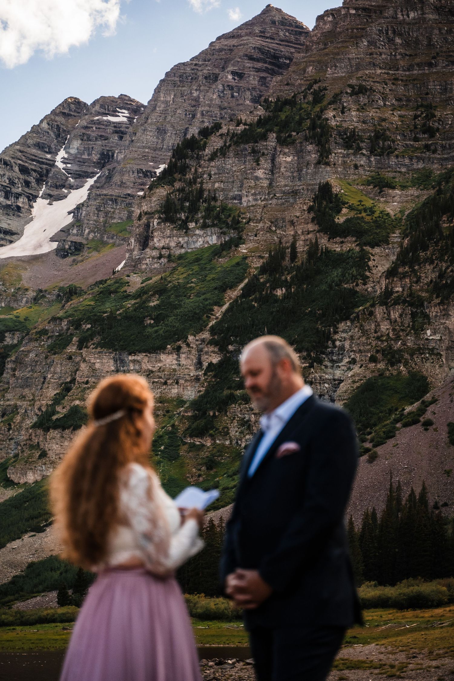 A dramatic mountain backdrop frames a ceremony with towering peaks and snow patches.