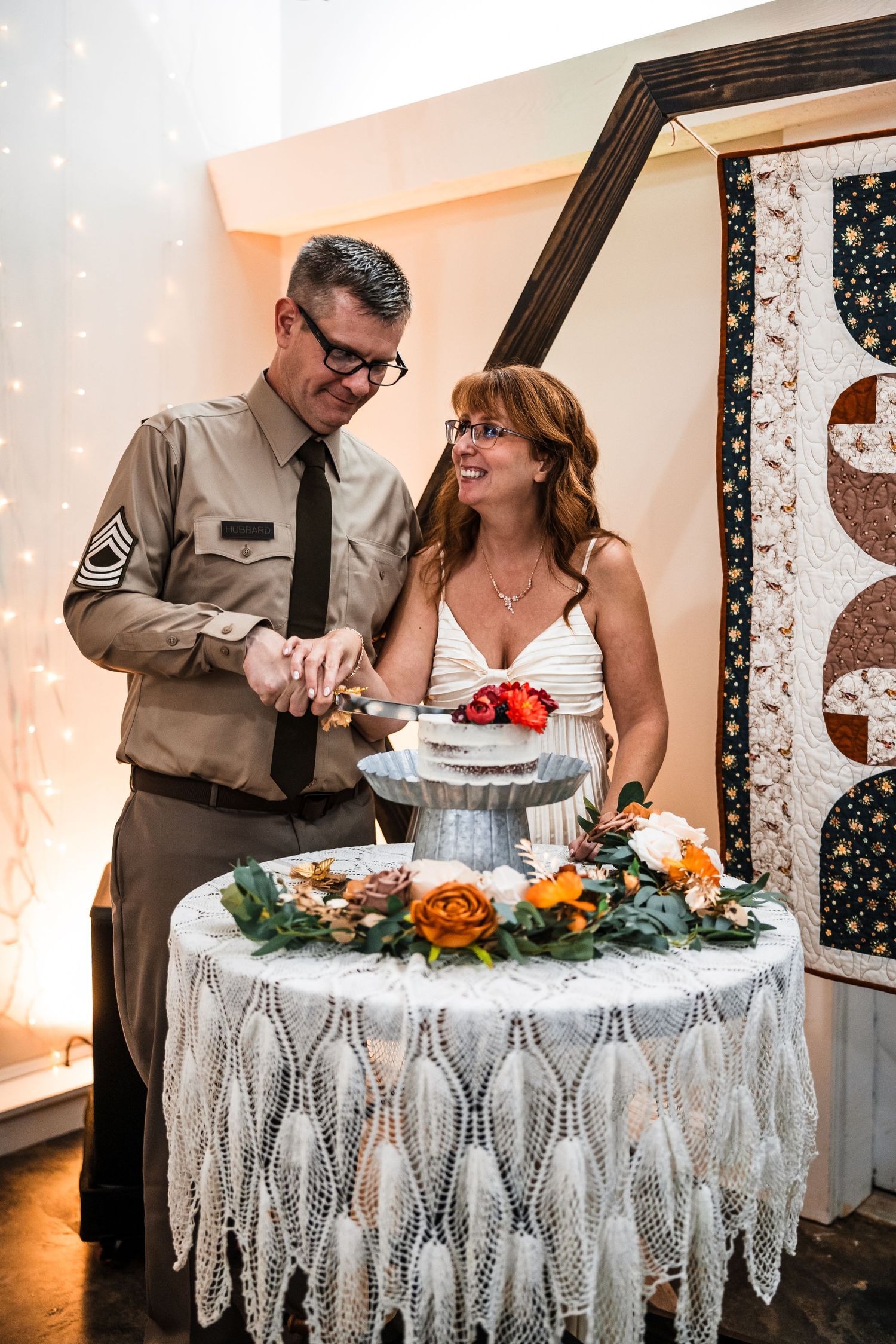 A couple cuts their wedding cake decorated with white lace and floral accents at their reception.