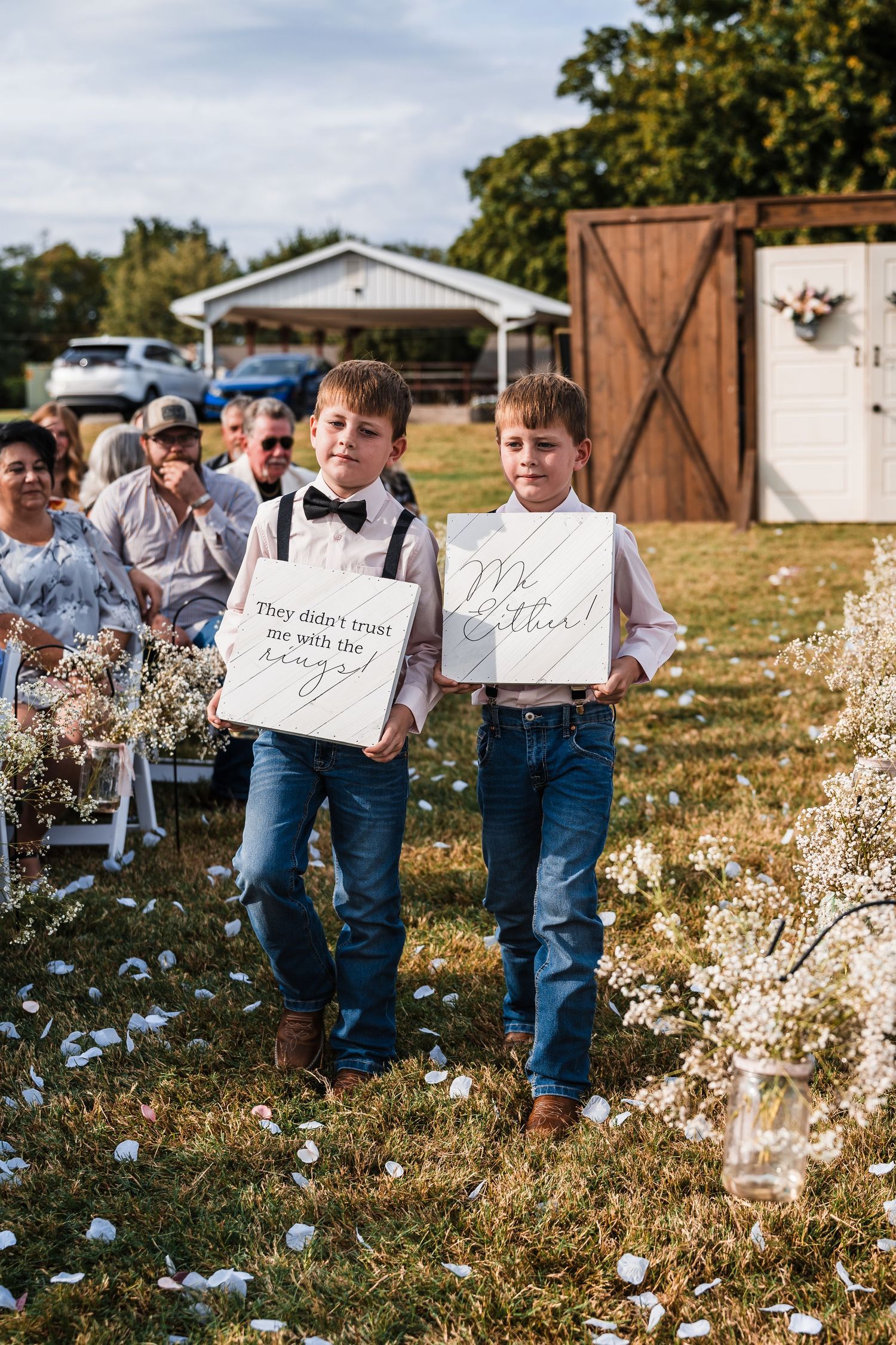 Ring bearers hold decorative signs while walking through a wildflower field.