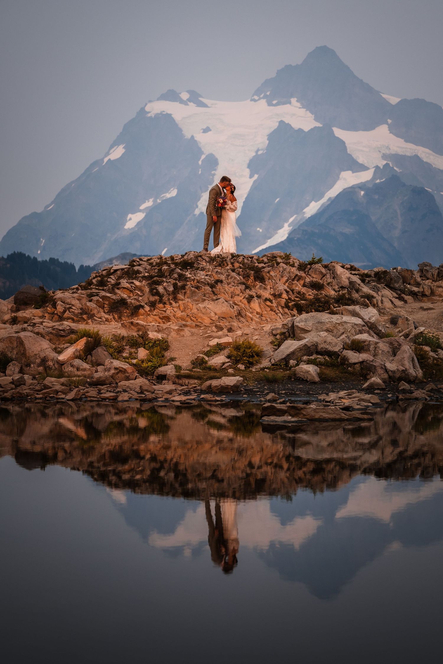 Mountain landscape with rocky outcrop reflected in still alpine lake at dusk.