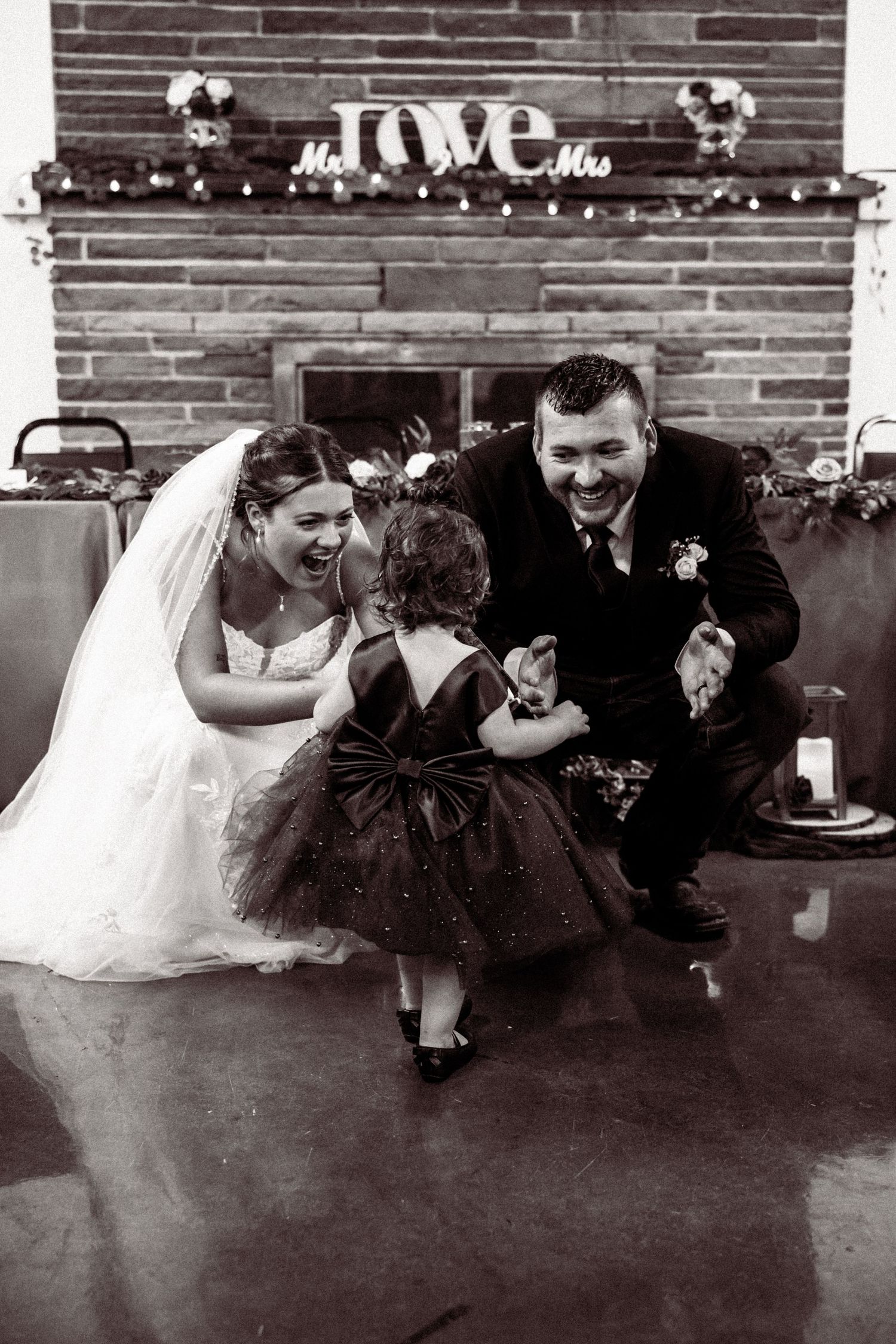 Wedding party poses playfully against a brick wall decorated with string lights.