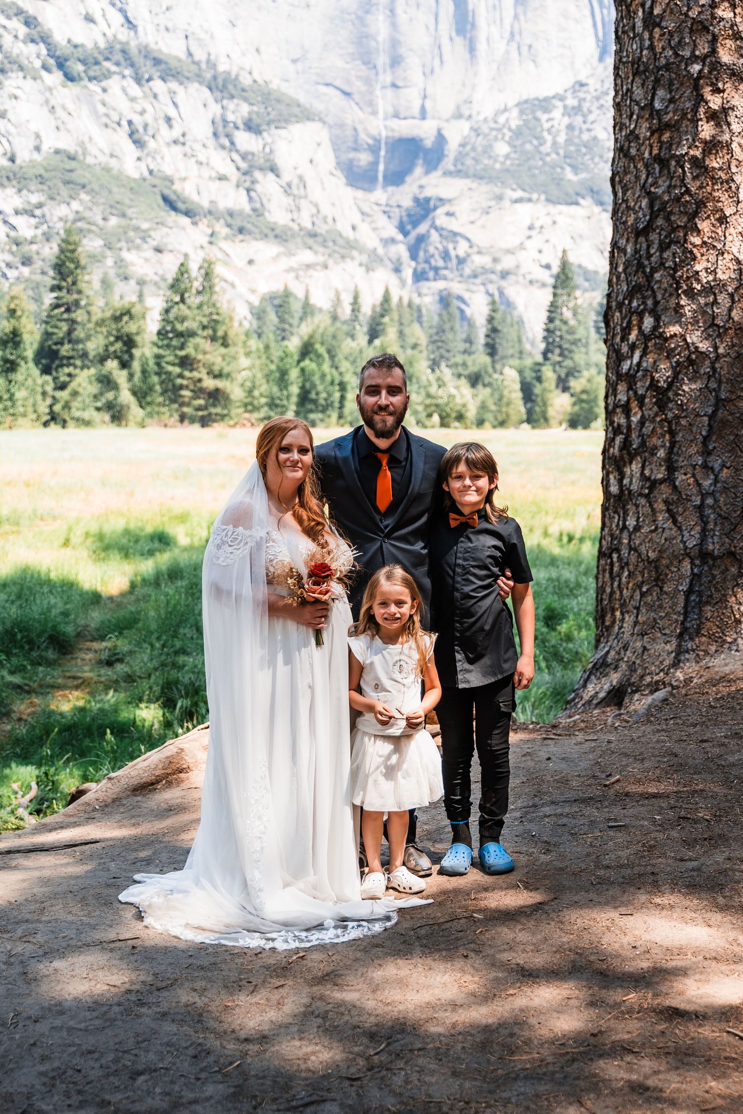 A wedding portrait taken in front of majestic mountain cliffs in an outdoor park setting.