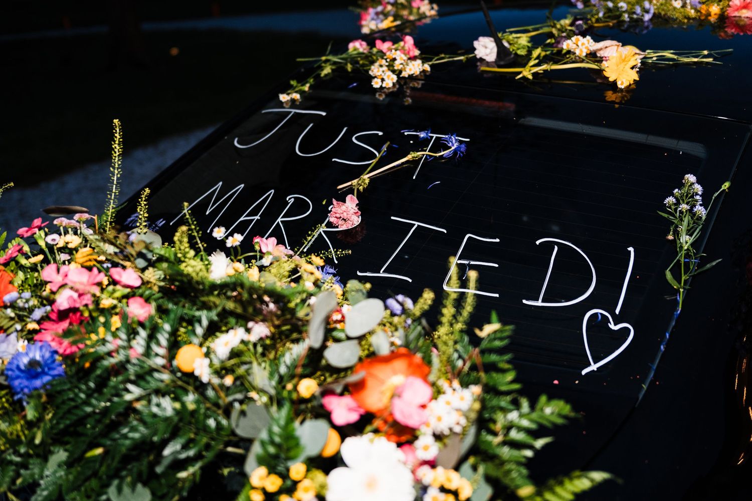 Just married sign written on car roof surrounded by colorful wedding flowers.