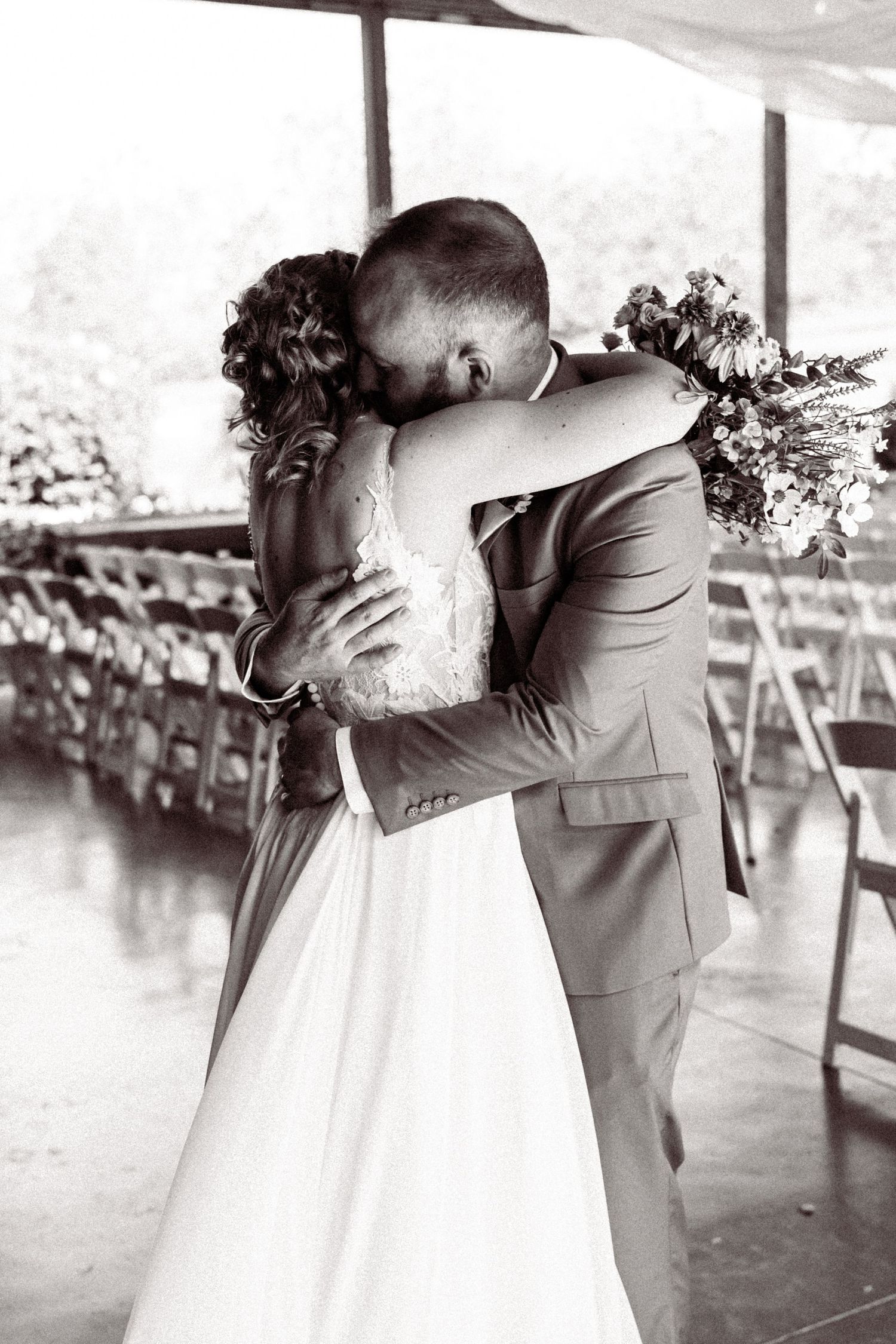 Black and white photo of bride and groom sharing emotional first kiss embrace at wedding ceremony.