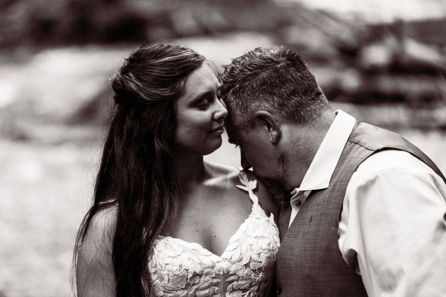 Black and white romantic portrait of bride and groom touching foreheads tenderly outdoors.