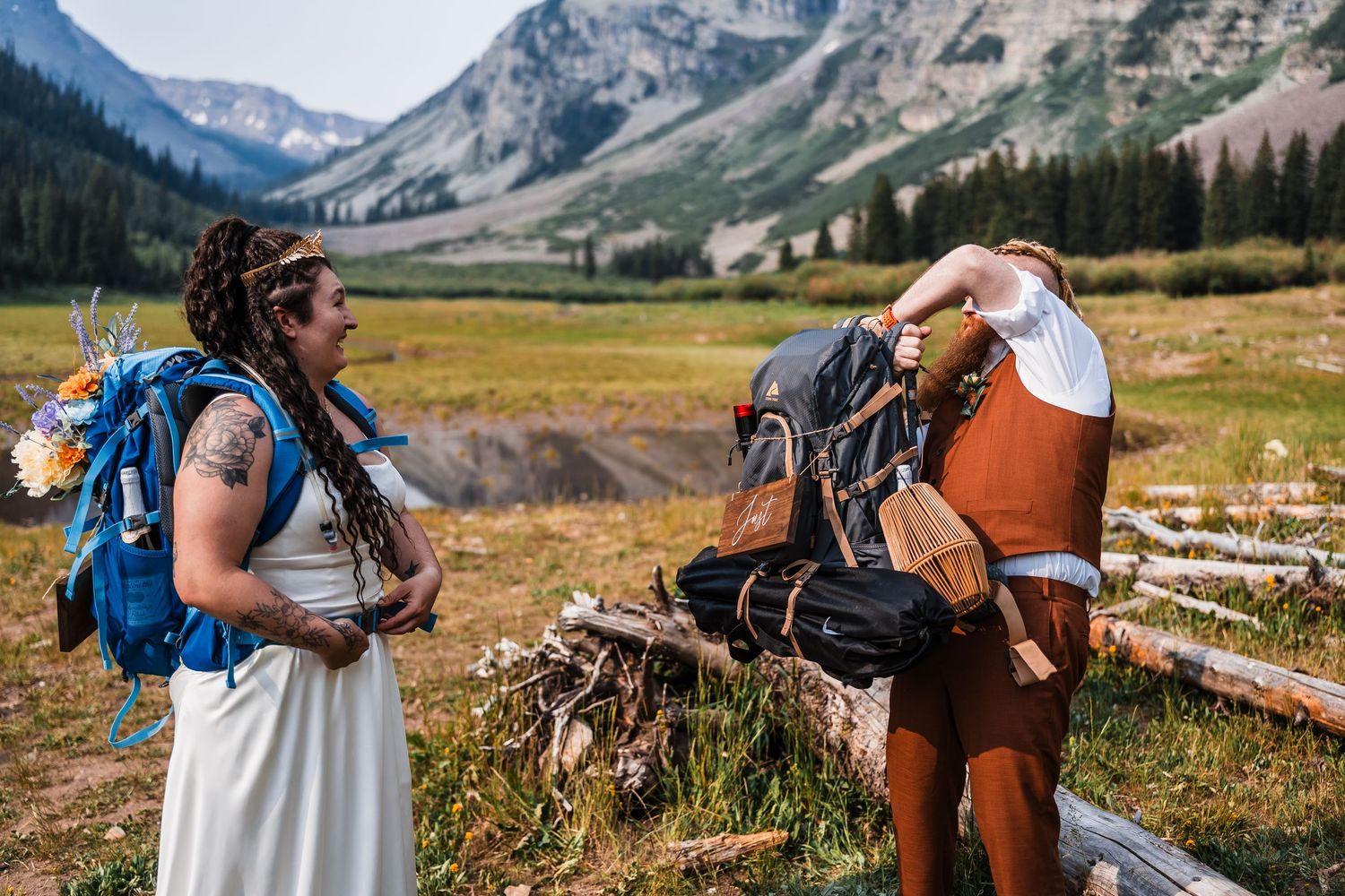 Bride and groom with hiking backpacks chat in alpine meadow before elopement hike.