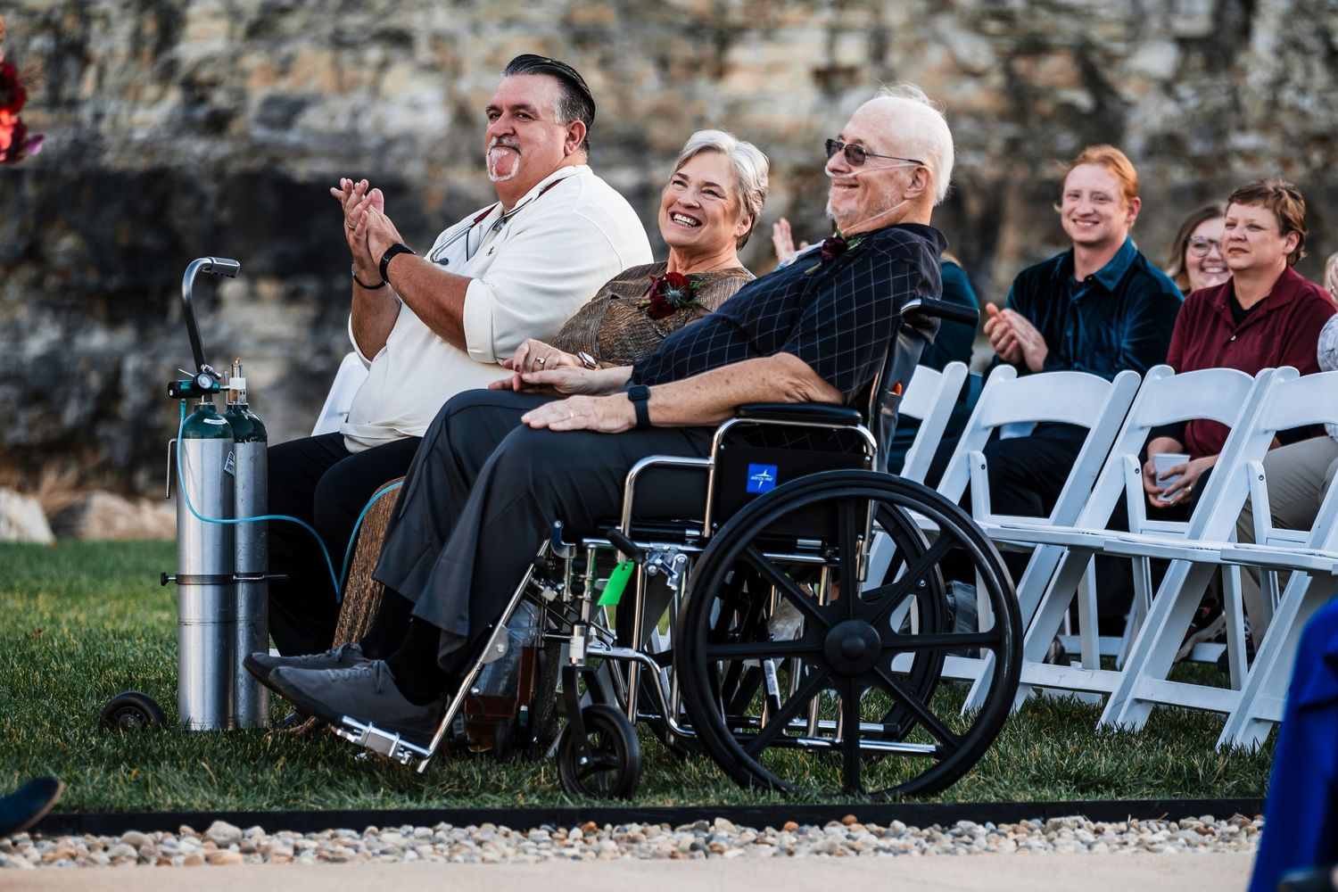 Wedding guests enjoying ceremony with emotional reactions while seated in white folding chairs.
