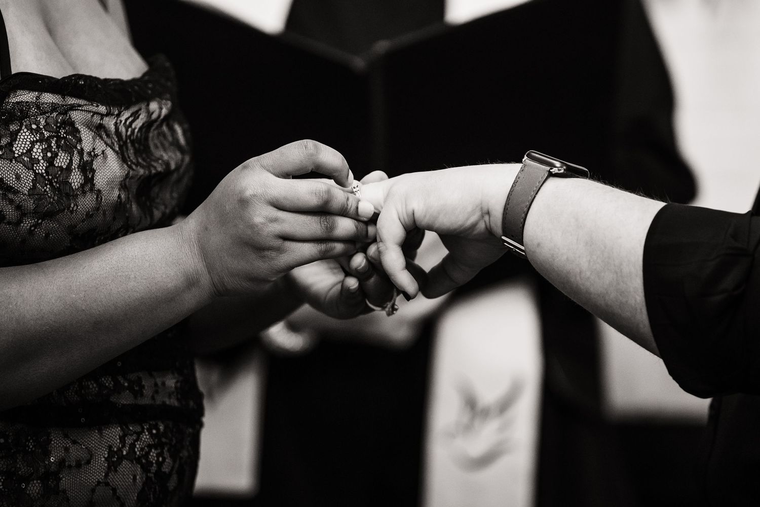 Black and white close-up photo of hands exchanging rings during an intimate wedding ceremony.