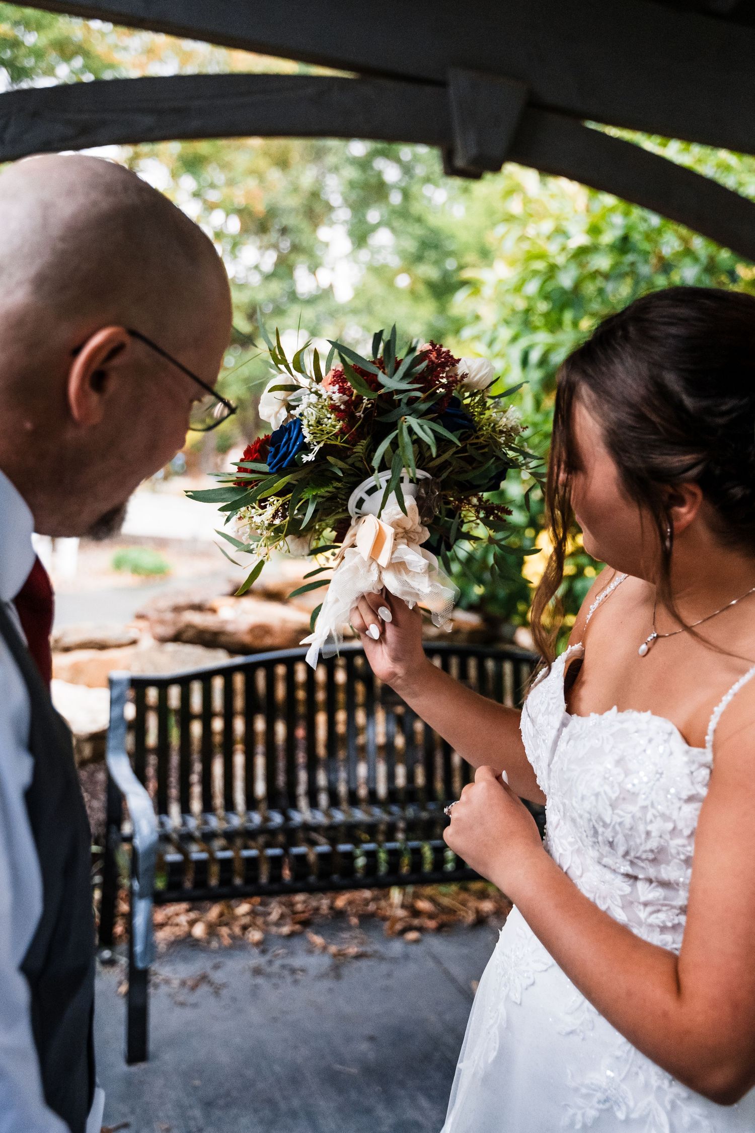 A couple shares an intimate moment under greenery at an outdoor wedding ceremony.