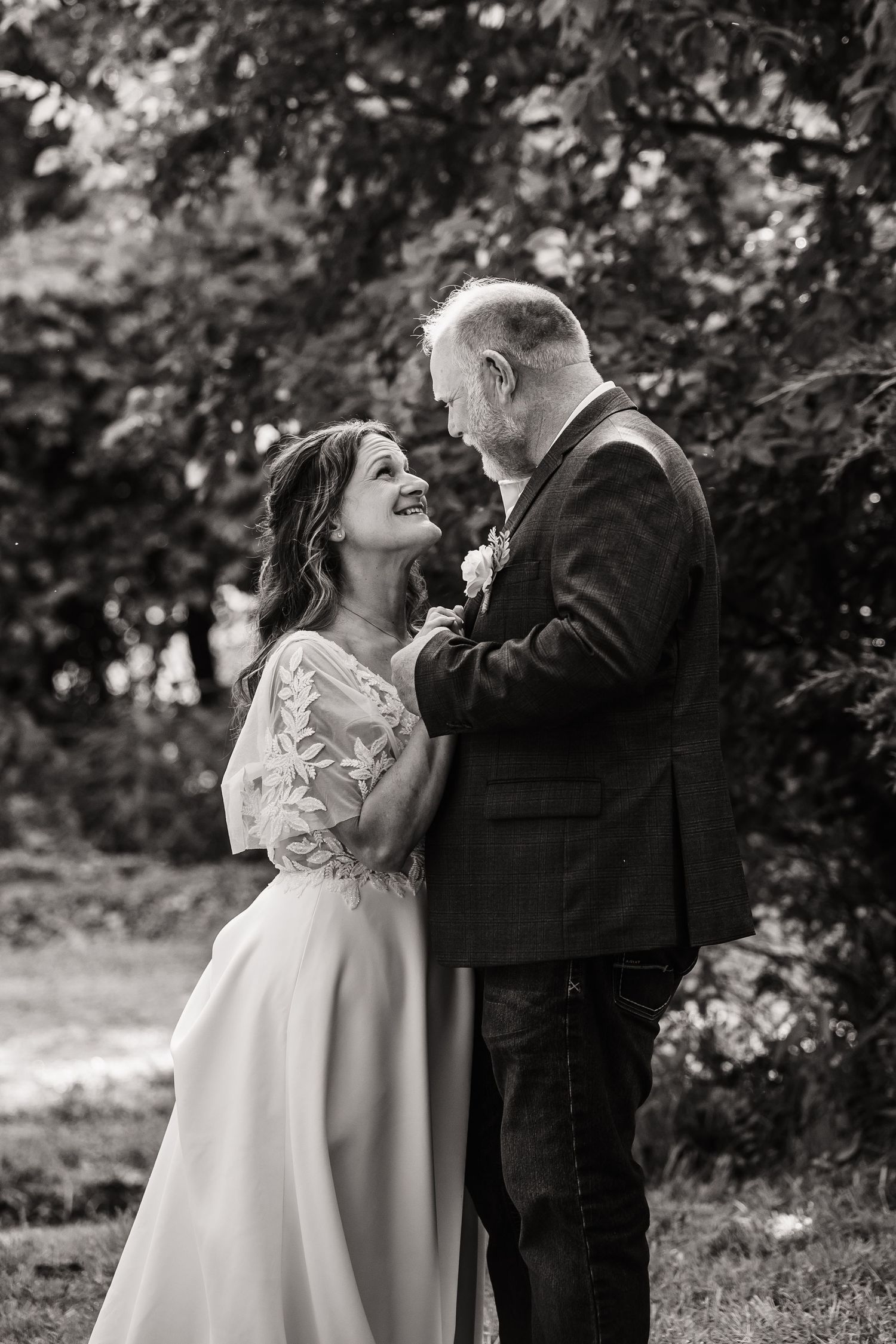 A romantic outdoor wedding portrait showing an intimate moment between newlyweds among garden foliage.