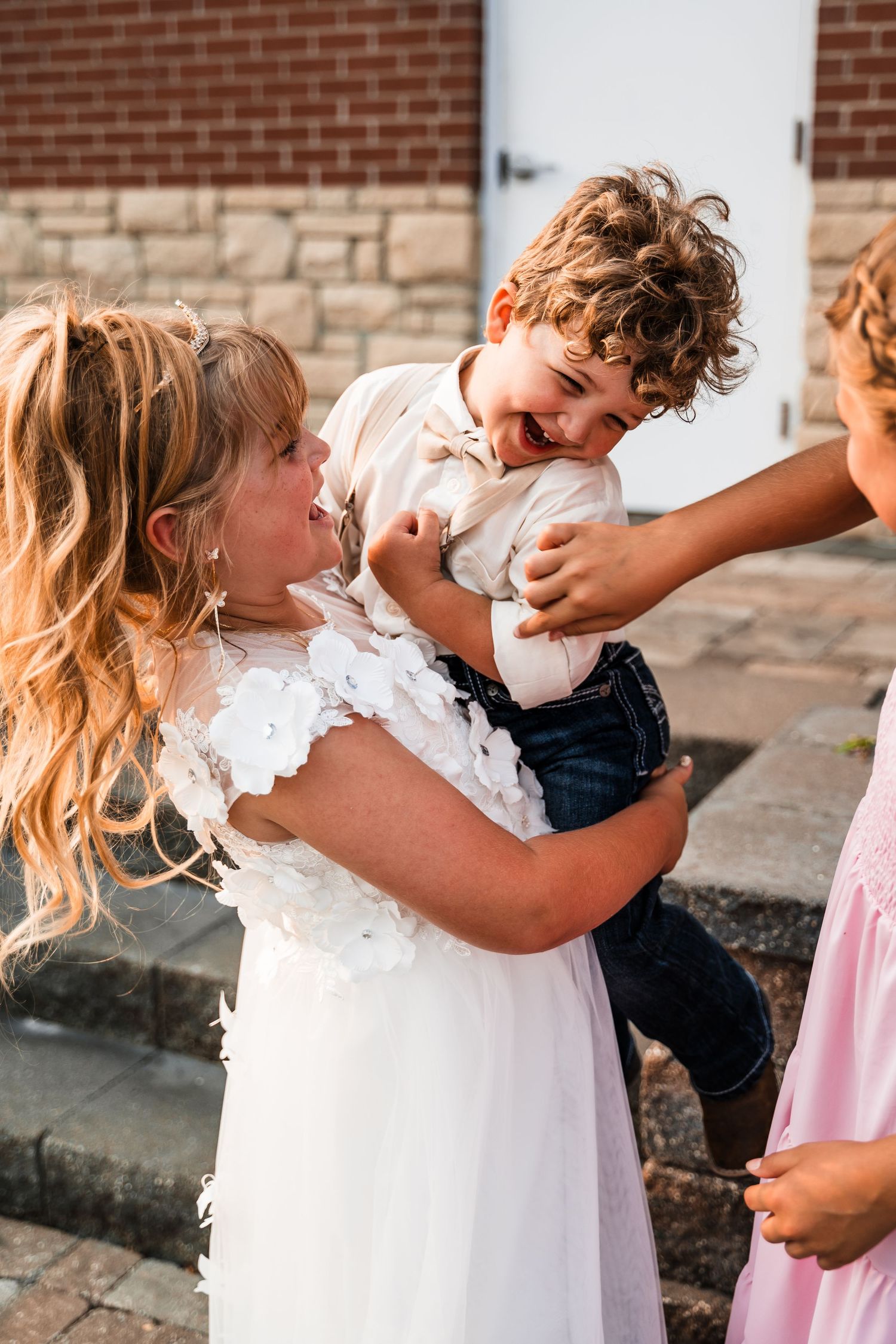 Sweet moment of children in white outfits hugging and playing during a wedding celebration.
