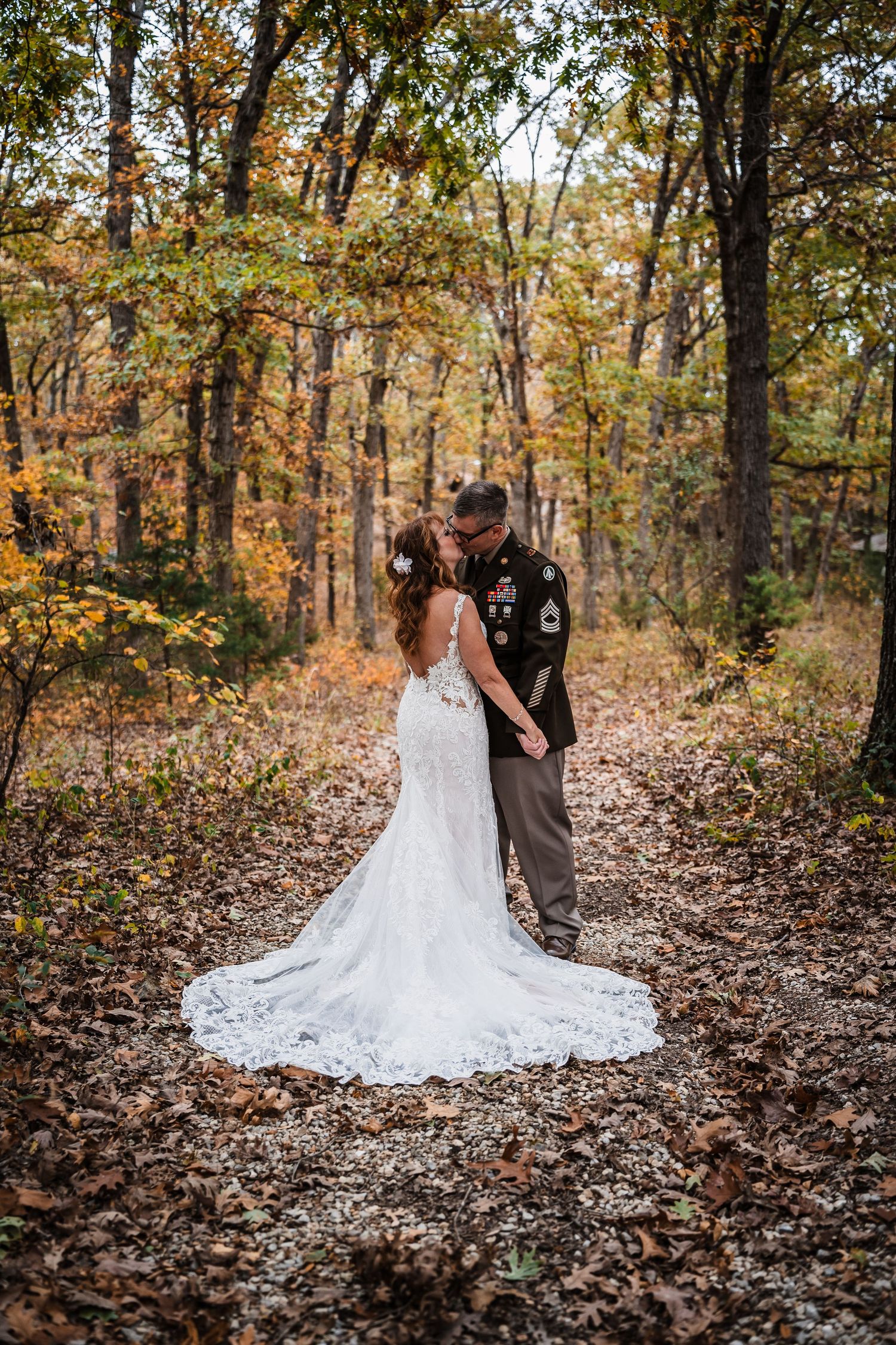 A couple in wedding attire shares an intimate moment among fall foliage and scattered leaves.