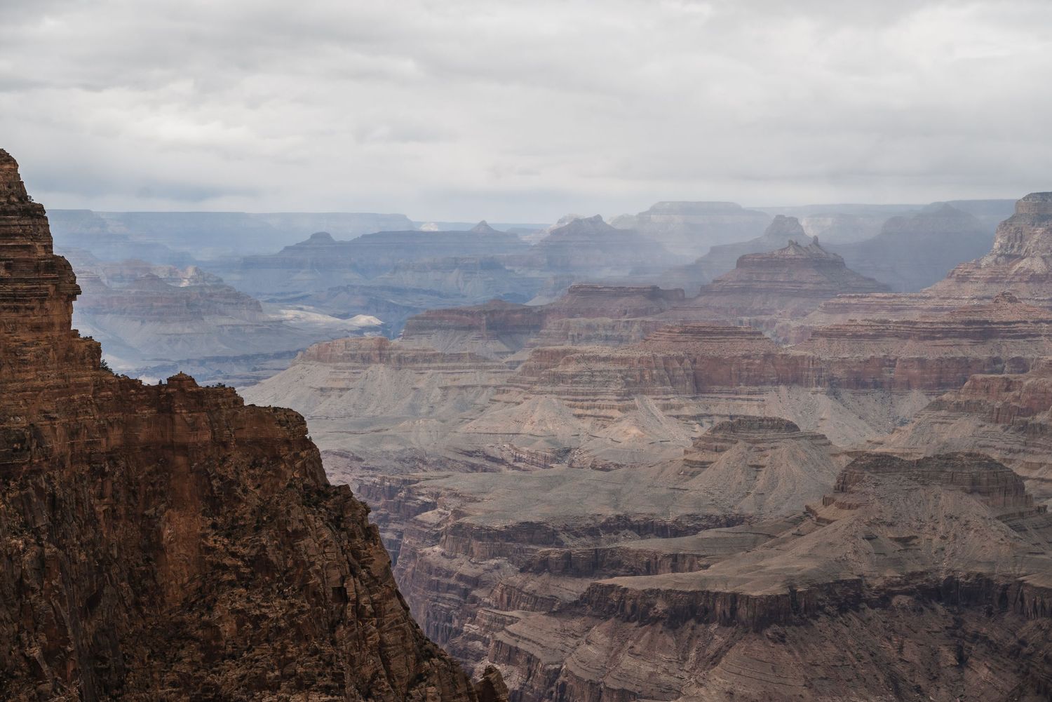 Dramatic desert landscape showcasing the layered cliffs and valleys of the Grand Canyon under cloudy skies.