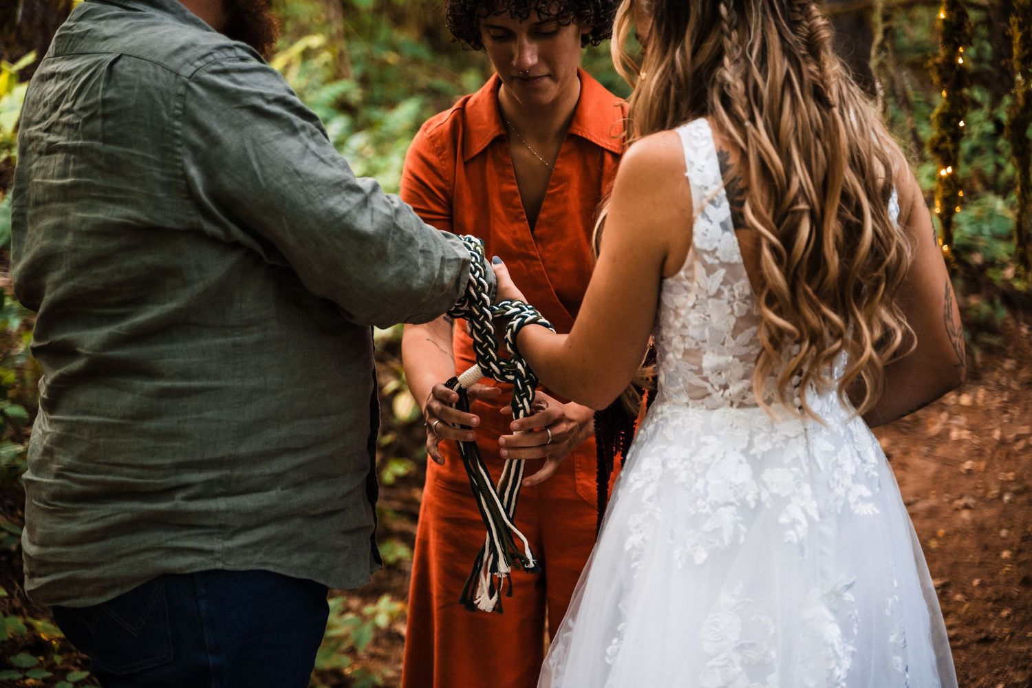 An intimate forest wedding ceremony with a minister in orange officiating under mossy branches.