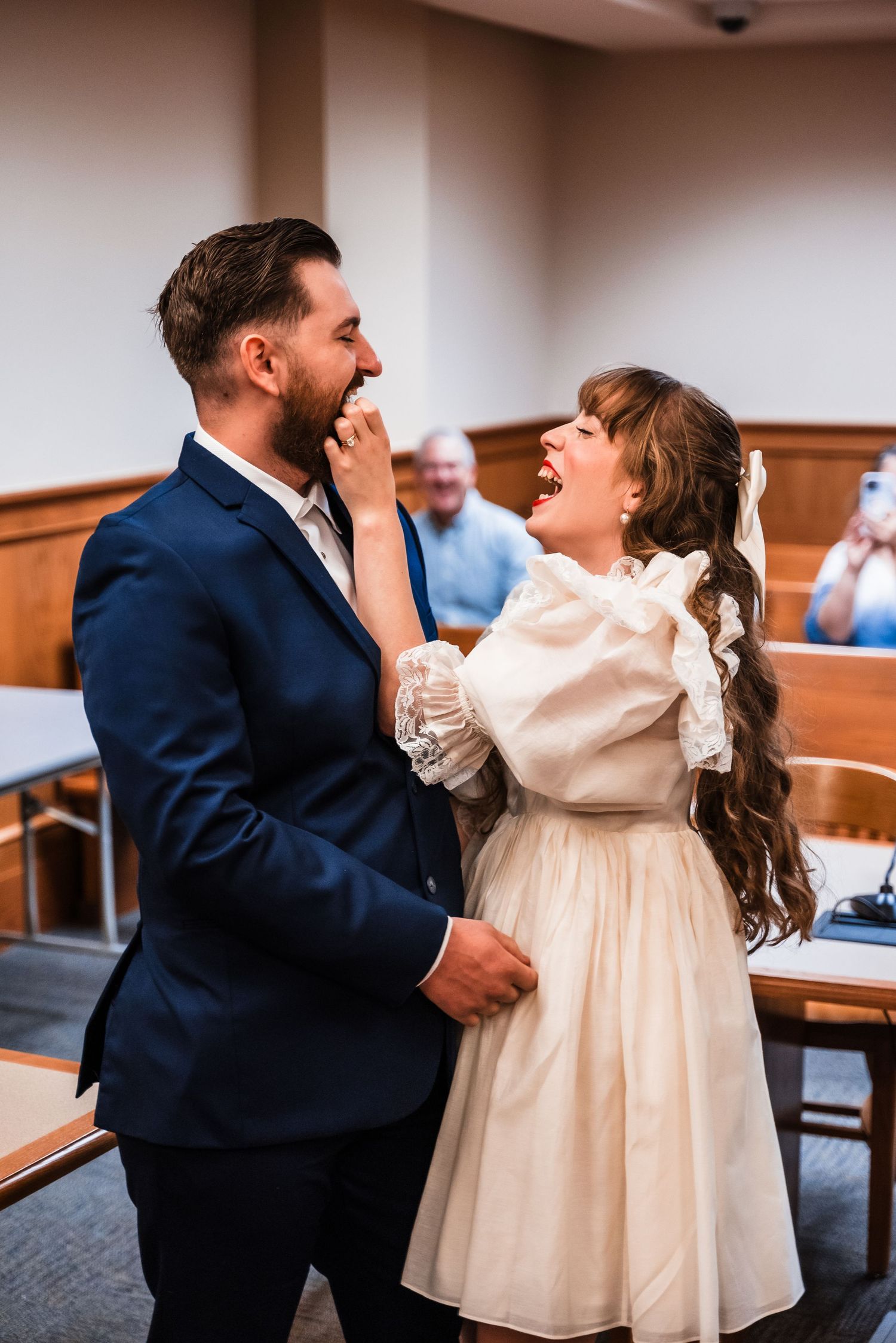Newlyweds share joyful moment during courthouse ceremony wearing vintage-inspired attire.