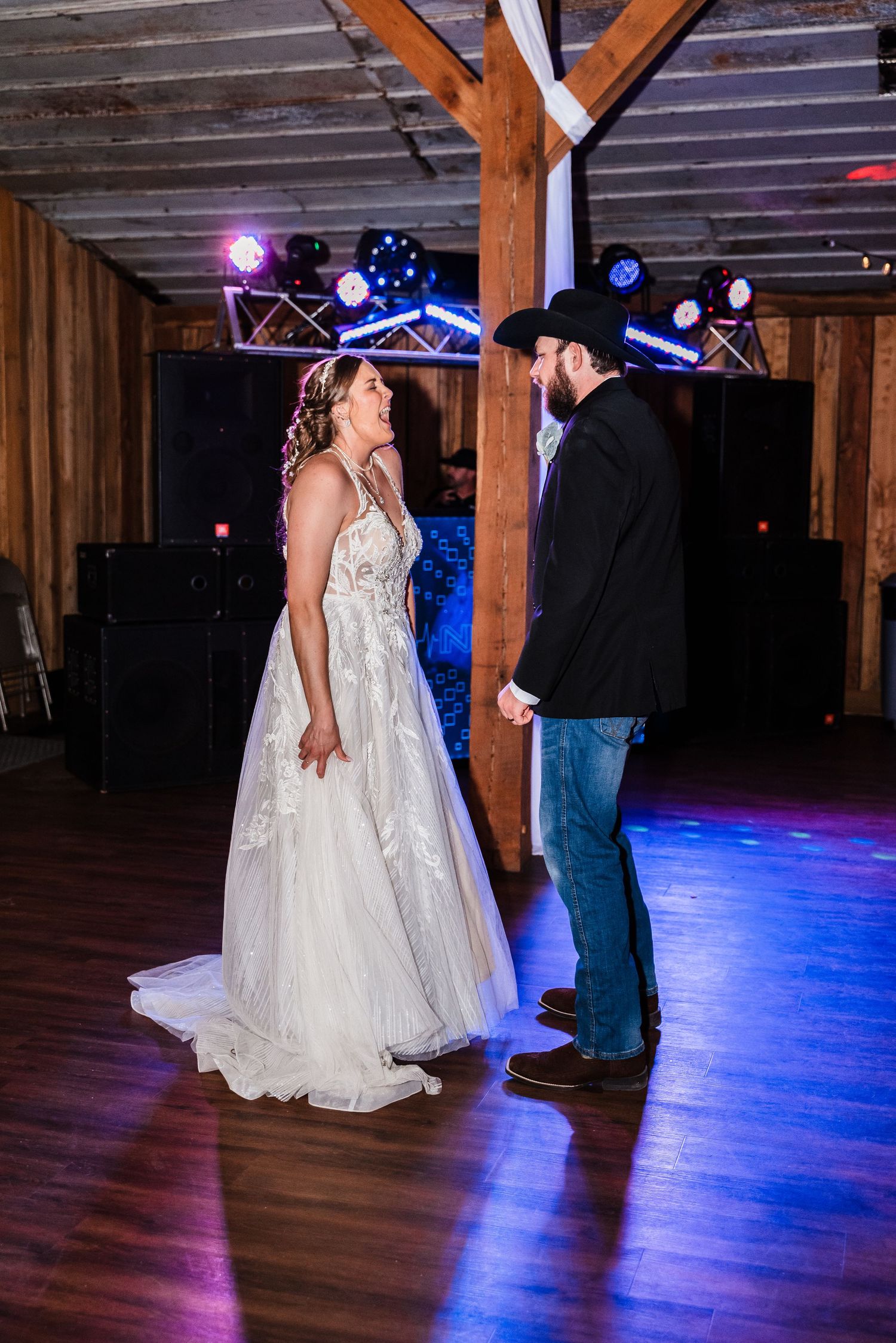A romantic moment between newlyweds dancing in a rustic barn with blue lighting effects.