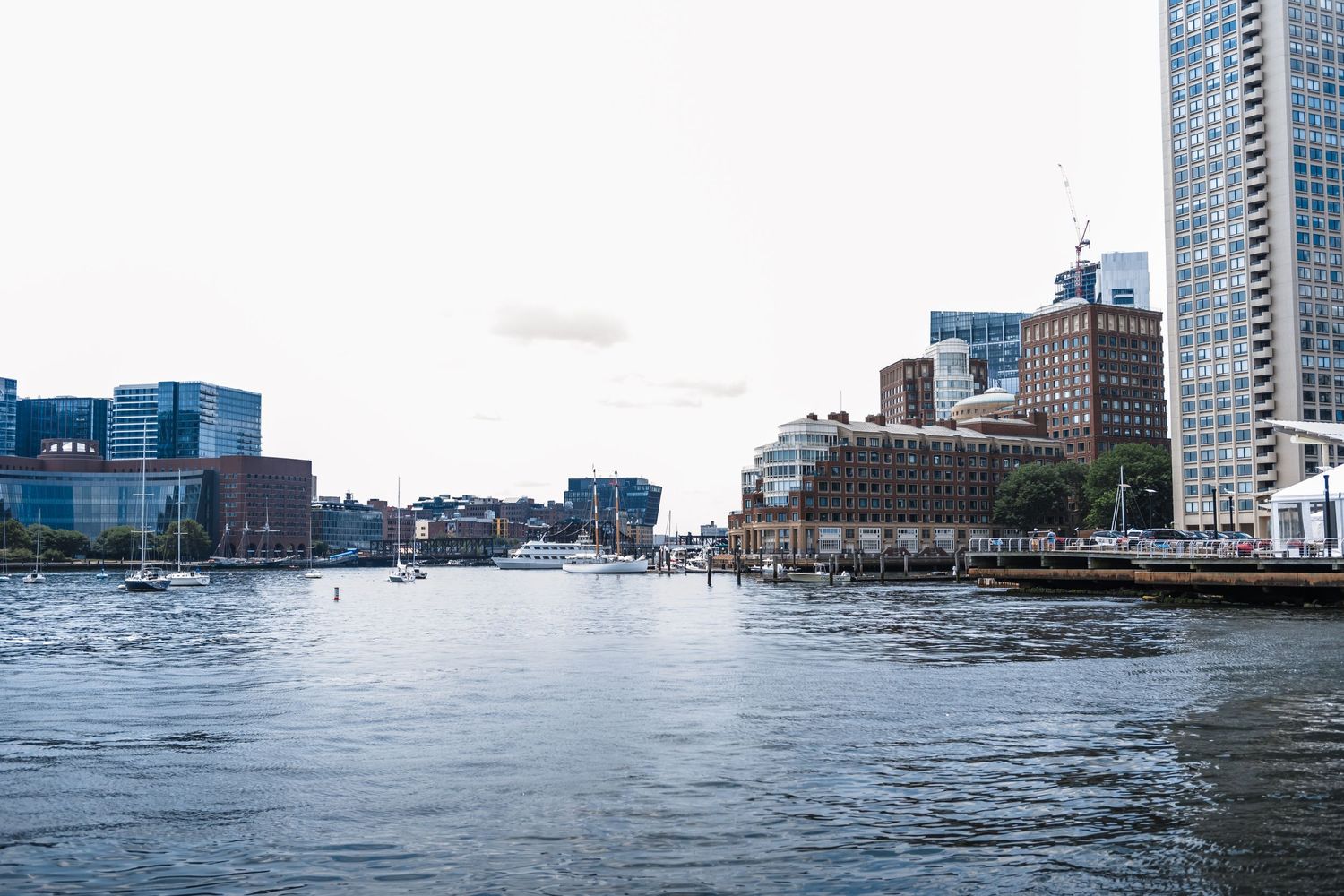 Waterfront cityscape with modern buildings and boats along an urban harbor on a cloudy day.