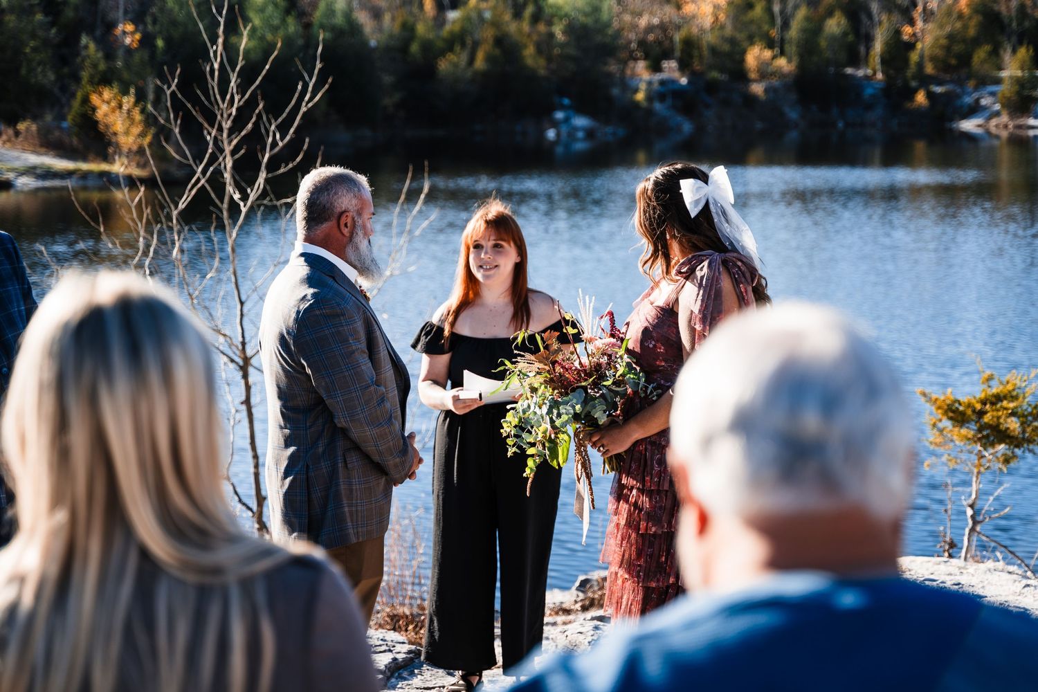 Small outdoor winter wedding ceremony taking place beside a serene lake.