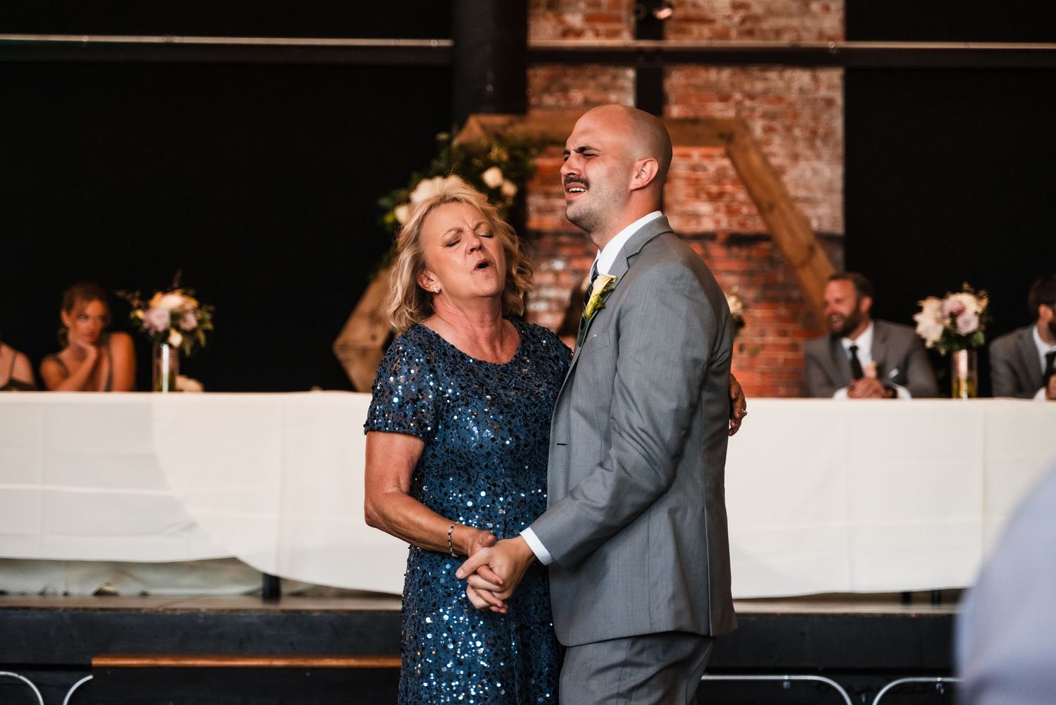A couple shares a romantic dance at their wedding reception, with the woman wearing a sparkly navy dress.