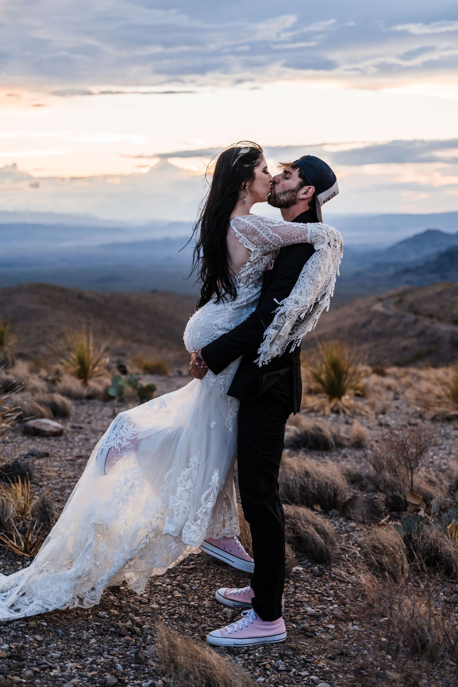 A joyful embrace between newlyweds on a mountain overlook during sunset.