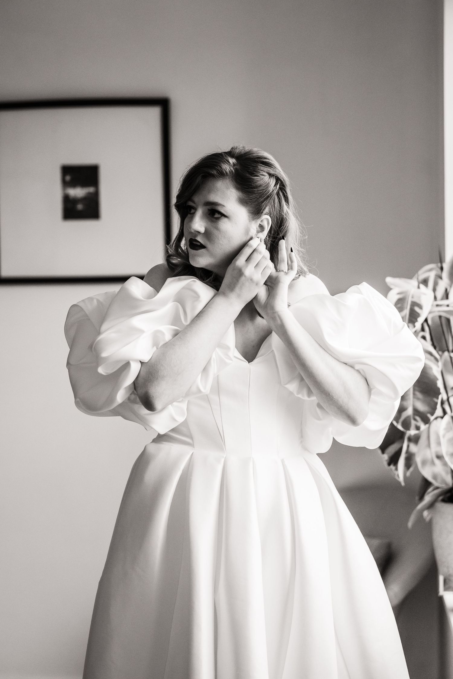 Elegant bride in white puffy-sleeved wedding gown adjusts her earrings.