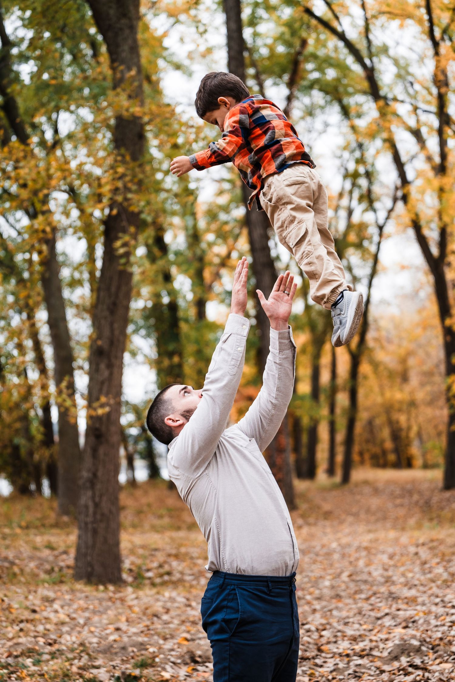 Playful moment captured as child is lifted high into air among fall foliage.