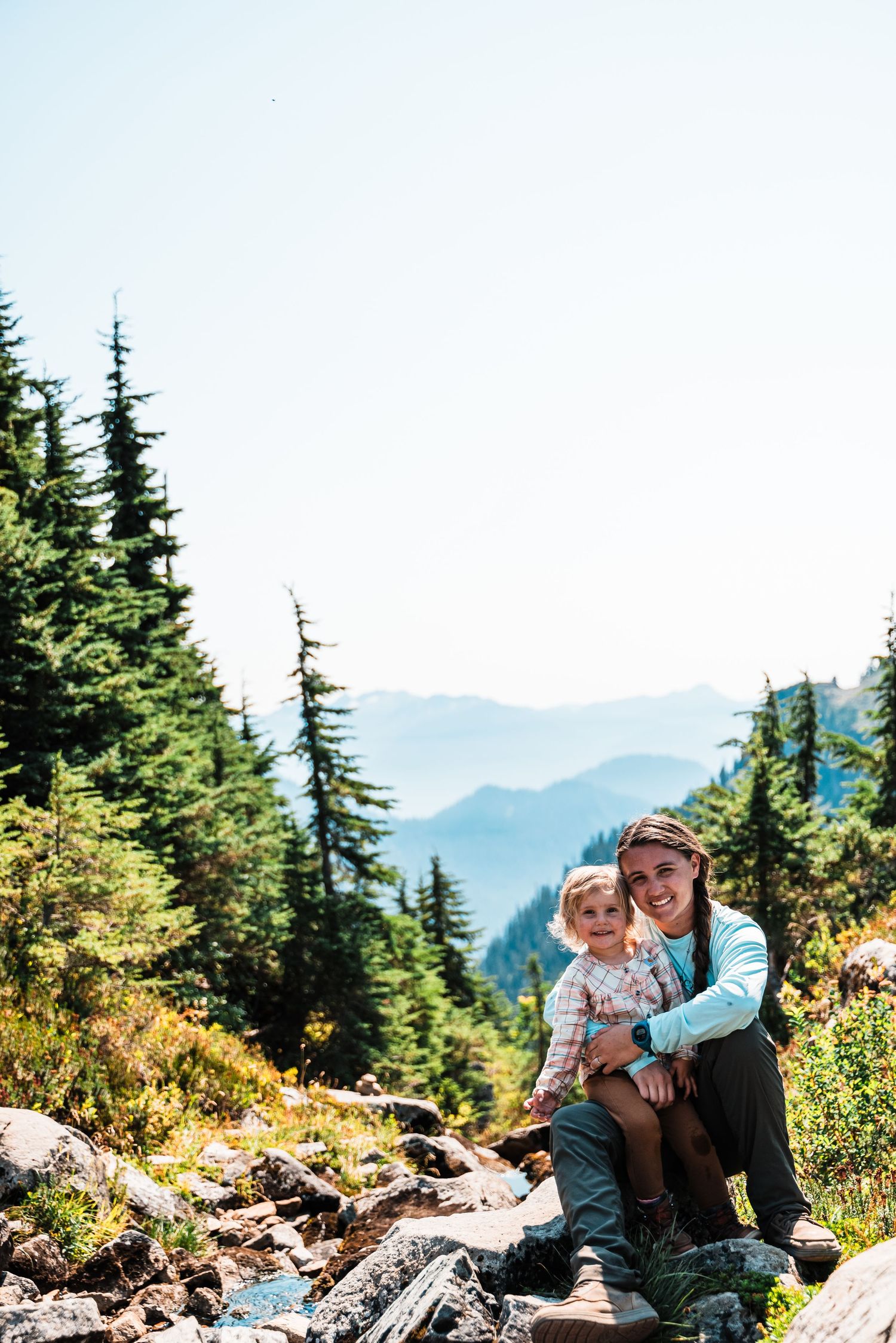 People resting on a rocky mountain overlook surrounded by evergreen trees.