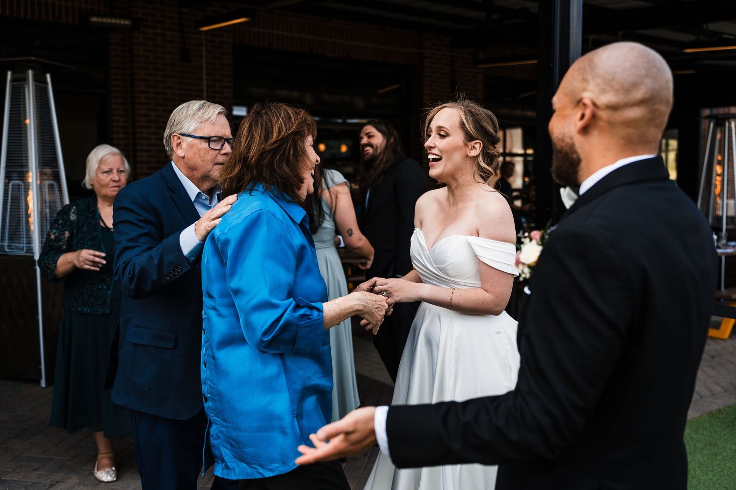 Bride and groom joyfully greet guests during outdoor wedding reception on a patio.
