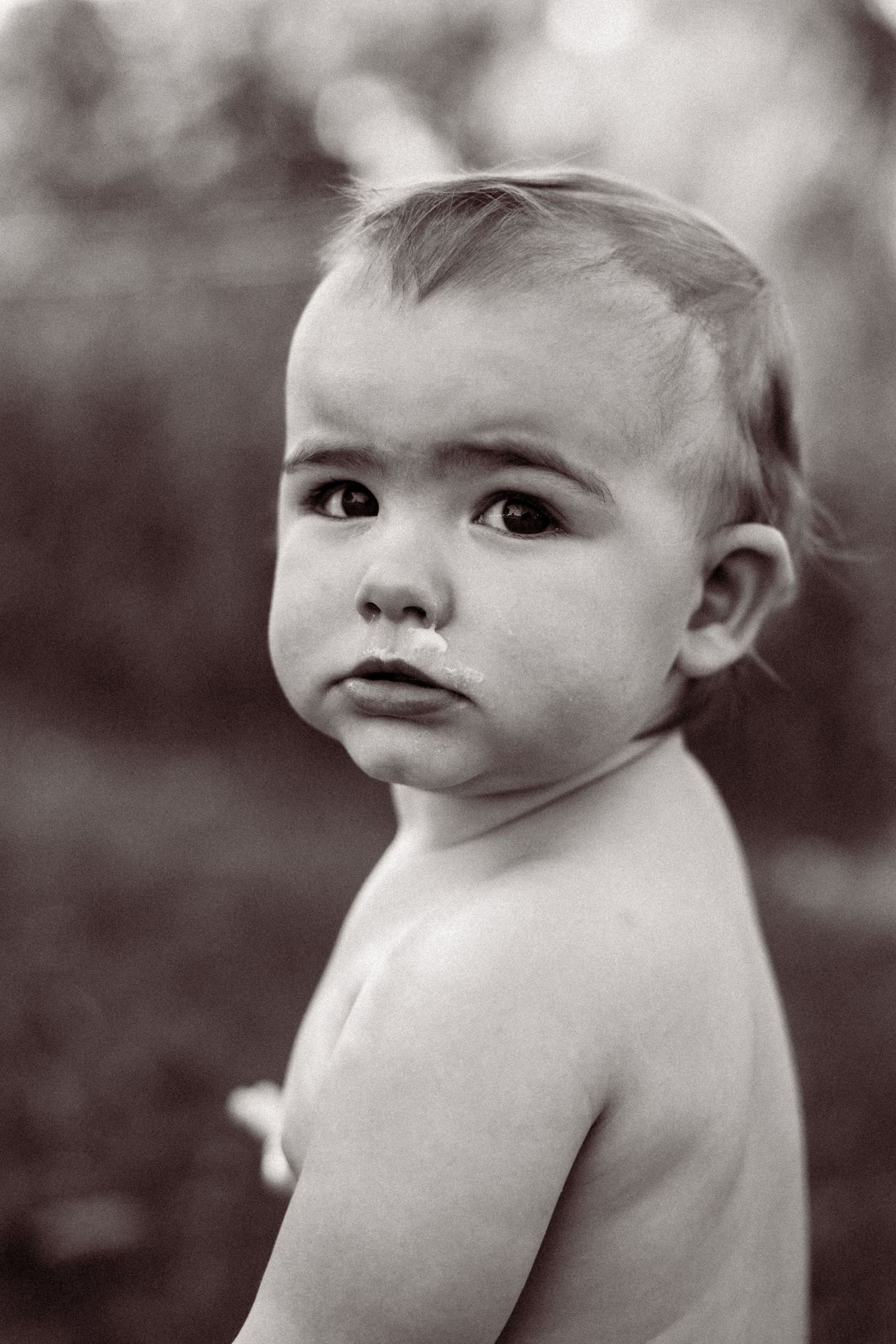 Black and white portrait of a small child looking over their bare shoulder with an innocent expression.