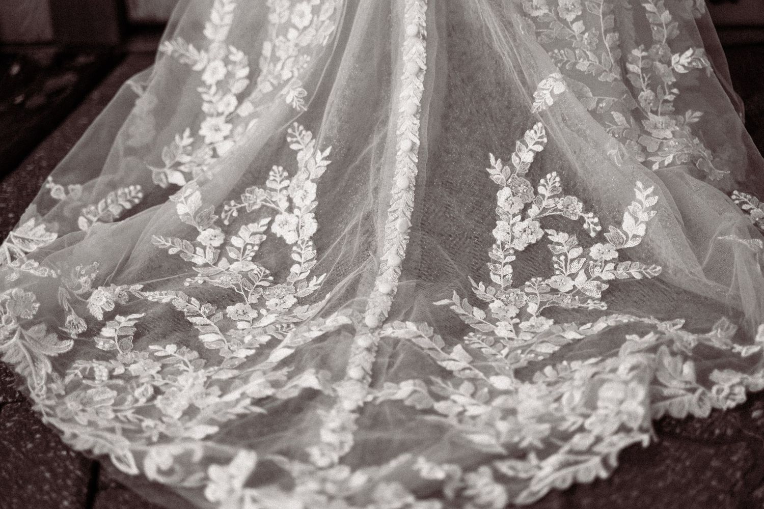 Close-up of elegant white lace wedding dress fabric with intricate floral embroidery and delicate tulle overlay.