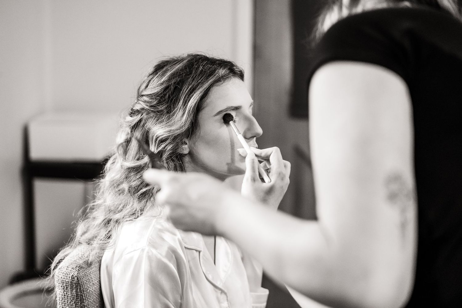 A black and white photo of a person in a light colored top getting their makeup done before an event.