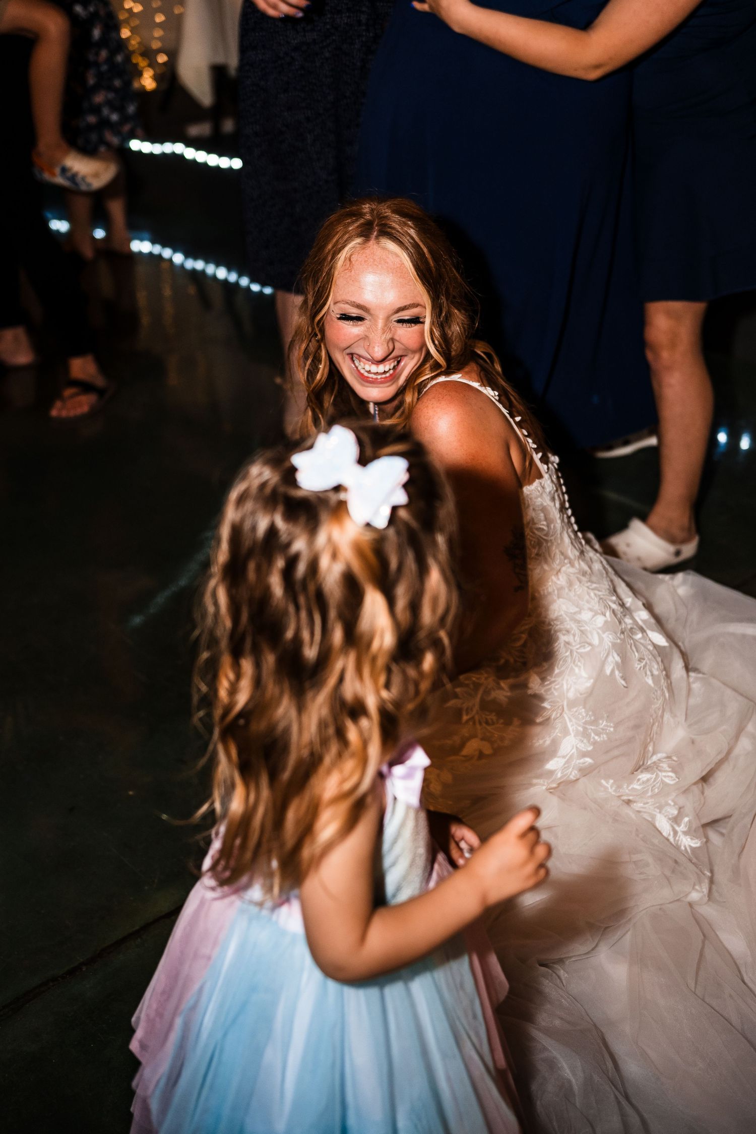 Bride and flower girl share playful laughing moment on dance floor at reception.
