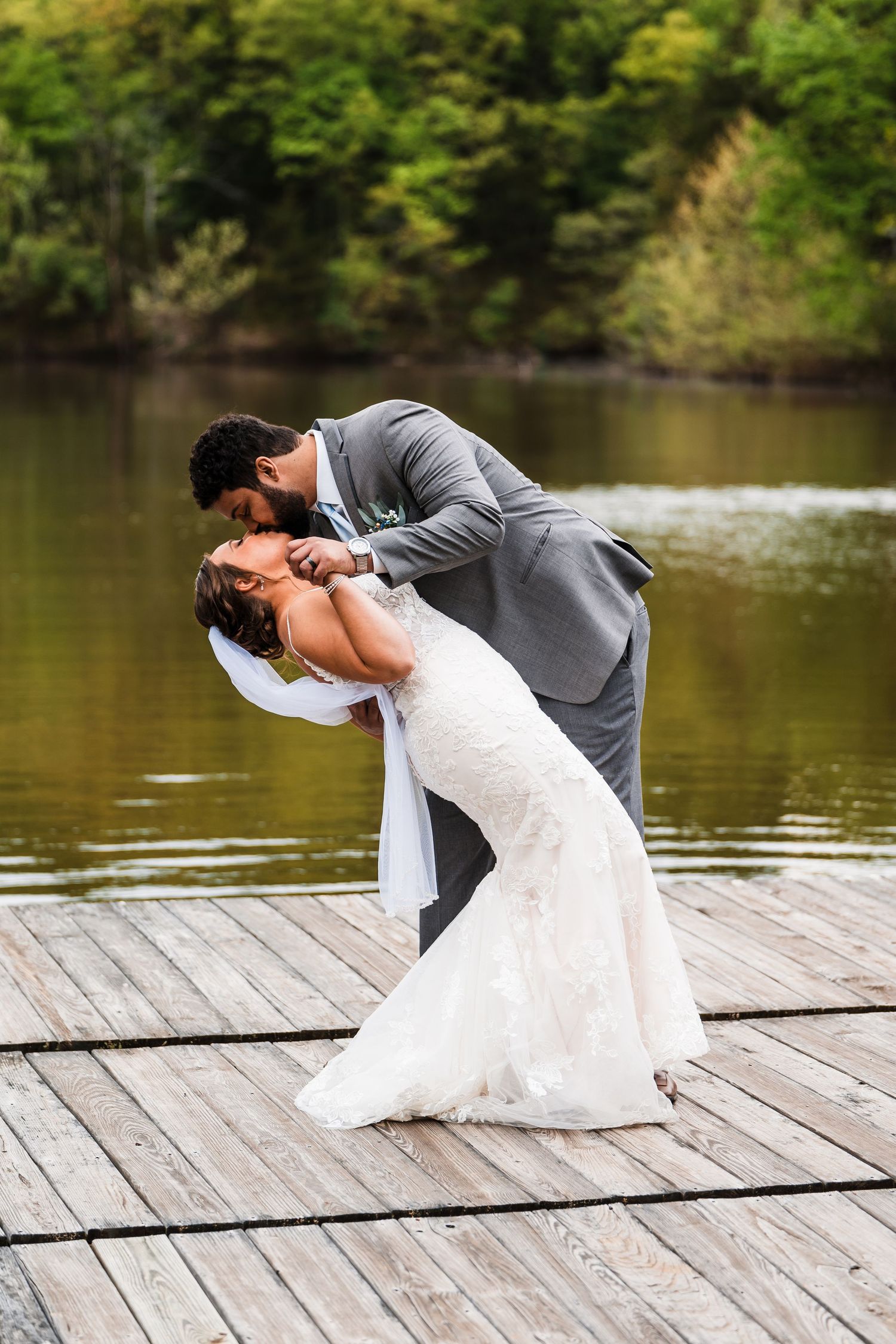 Romantic wedding couple sharing dramatic dip pose on lakeside dock.